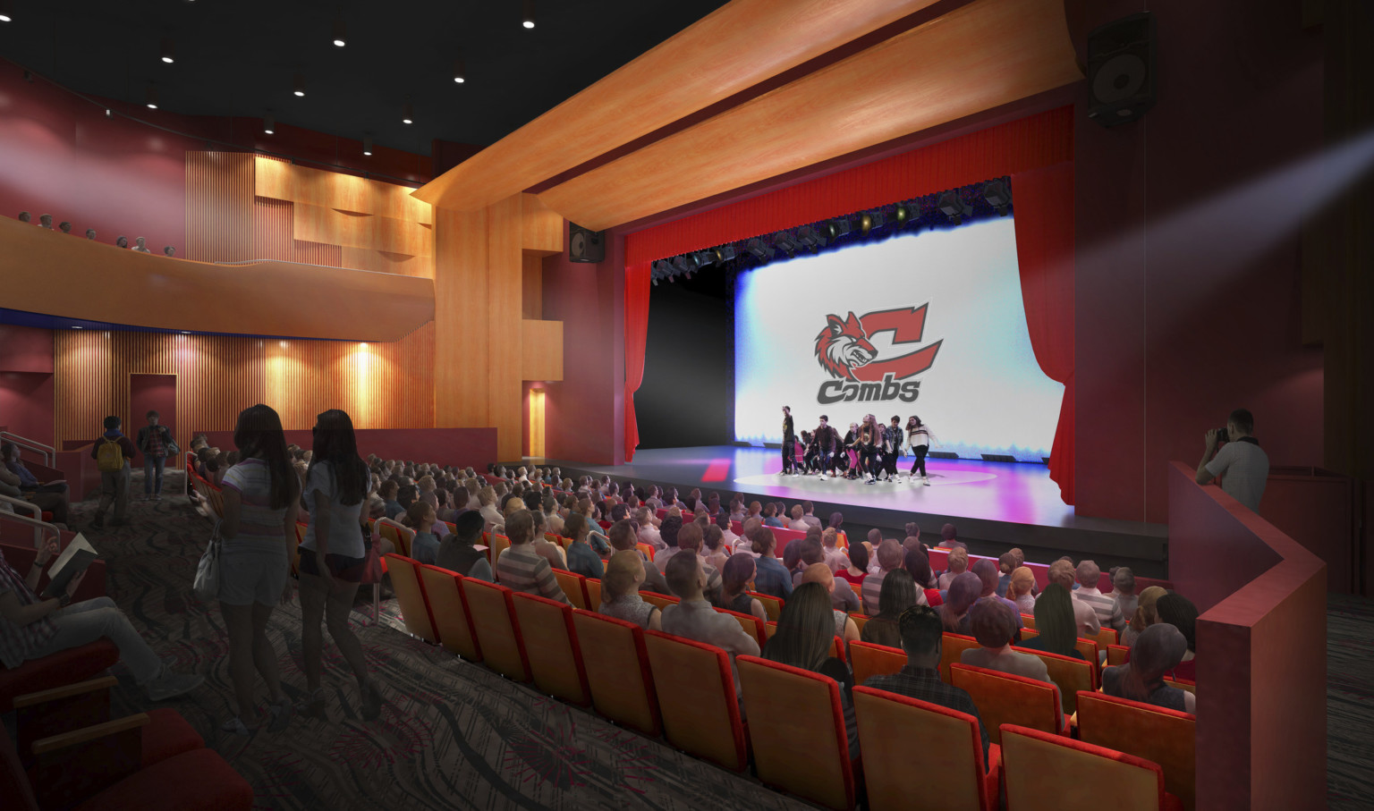 Red chairs with wooden backs inside J.O. Combs High School Auditorium with school logo on screen framed by red curtains