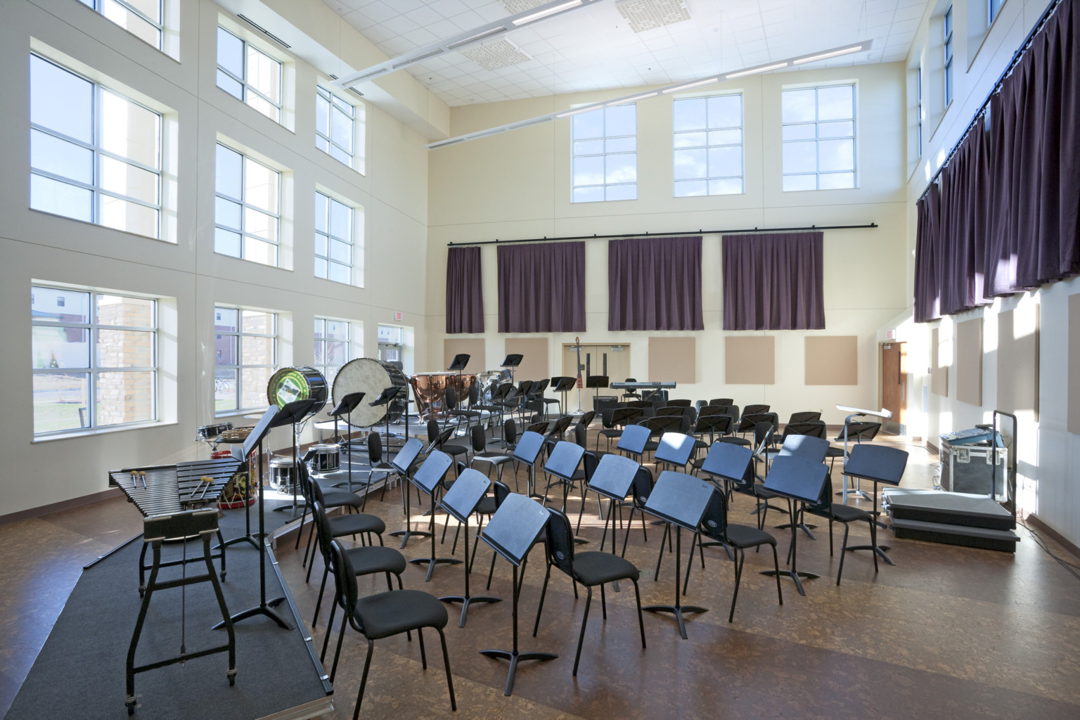 Band training room with rounded rows of plastic chairs with music stands in front of each in double height room with windows
