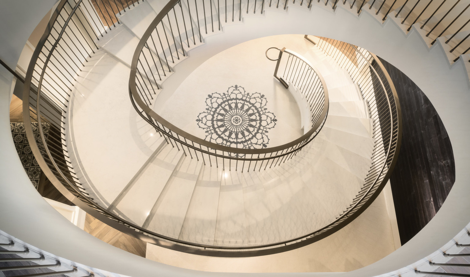 View from above of white spiral staircase with metallic railing. At the center of the floor in the spiral is a black mandala