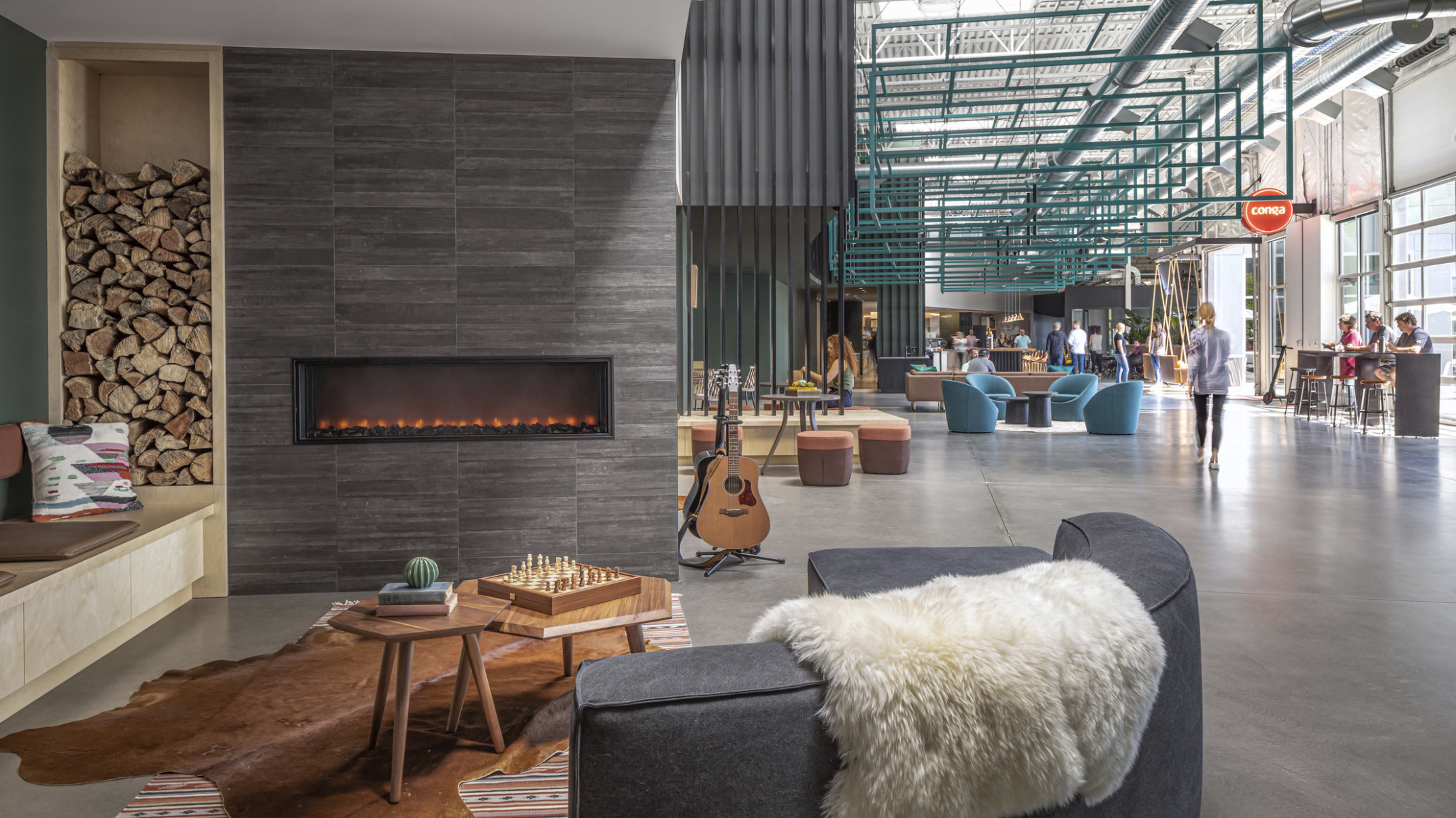 Conga Headquarters seating area with garage door windows on right wall. Couch at front left in front of fireplace