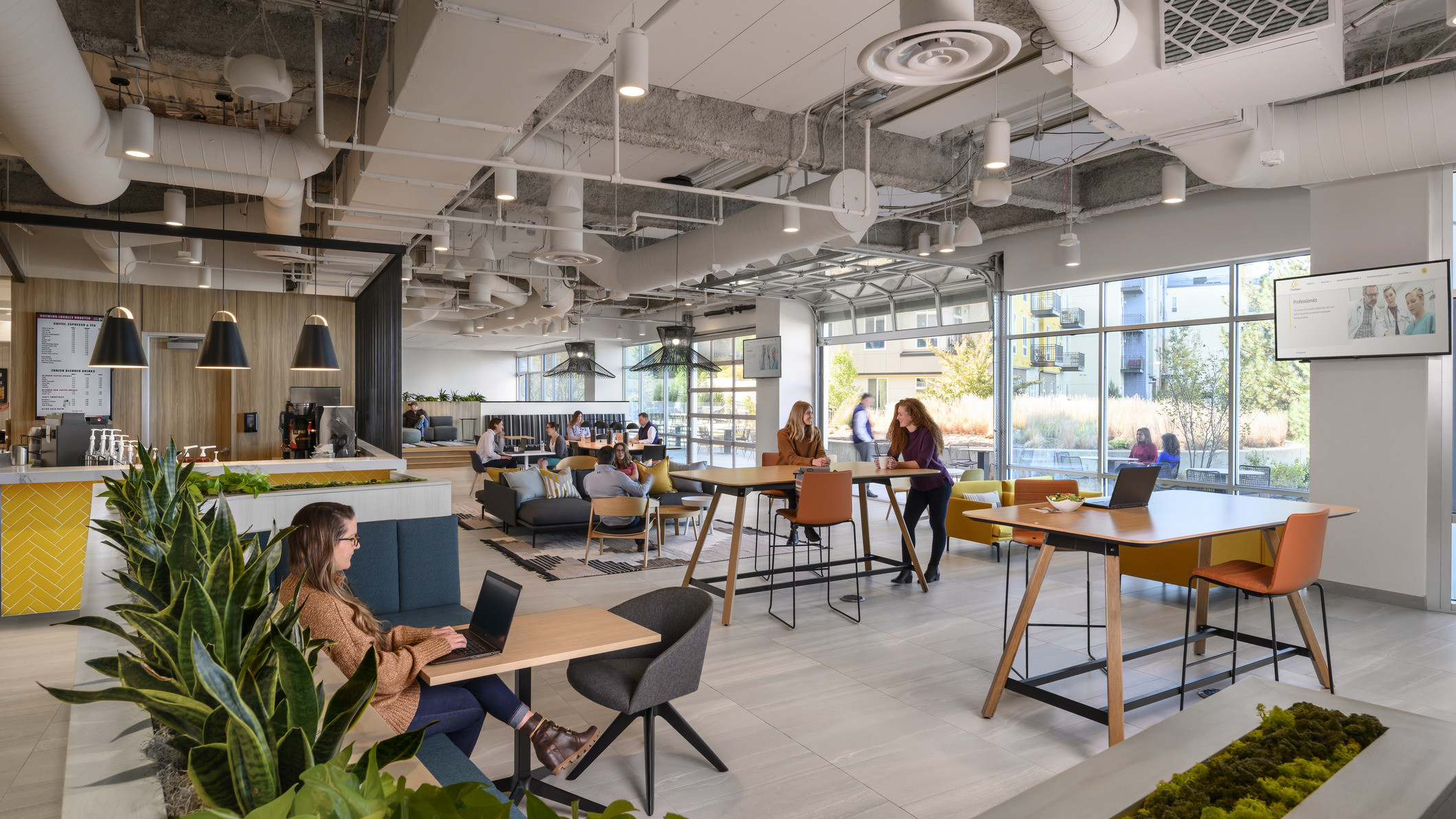 Mixed seating with tables in room with floor to ceiling windows with open garage style door, right. Coffee counter to left