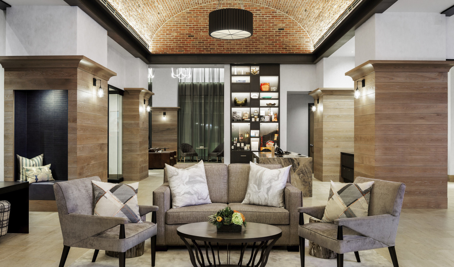 Seating area, beige couch with matching arm chairs around coffee table in white room with arching recessed brick ceiling