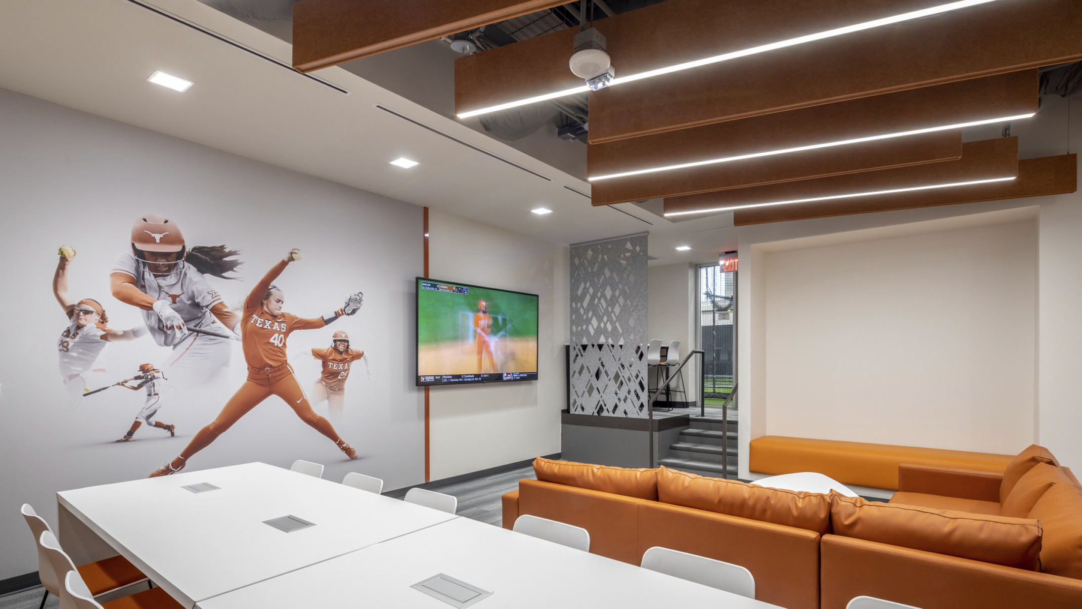 University of Texas Softball Development Facility interior. Softball mural on wall next to screen in front of orange couch