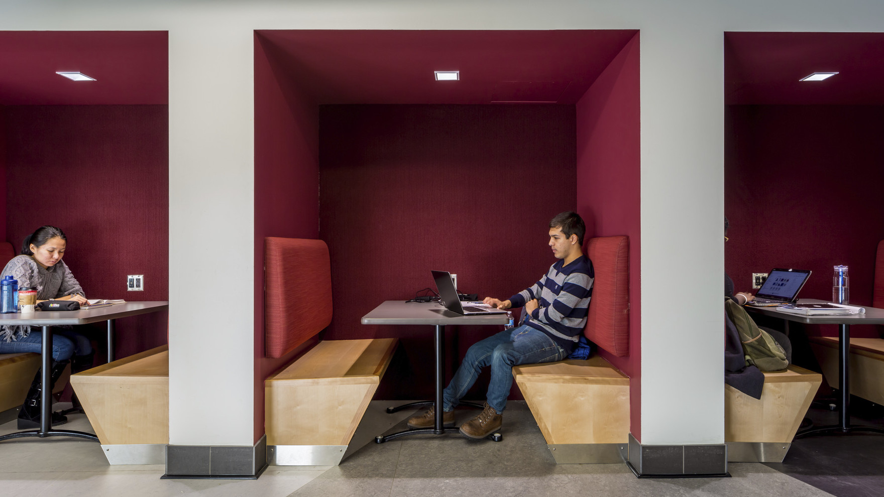 Tucked-in booths for collaboration with wood benches and dark red accents at the University of Minnesota cultural center