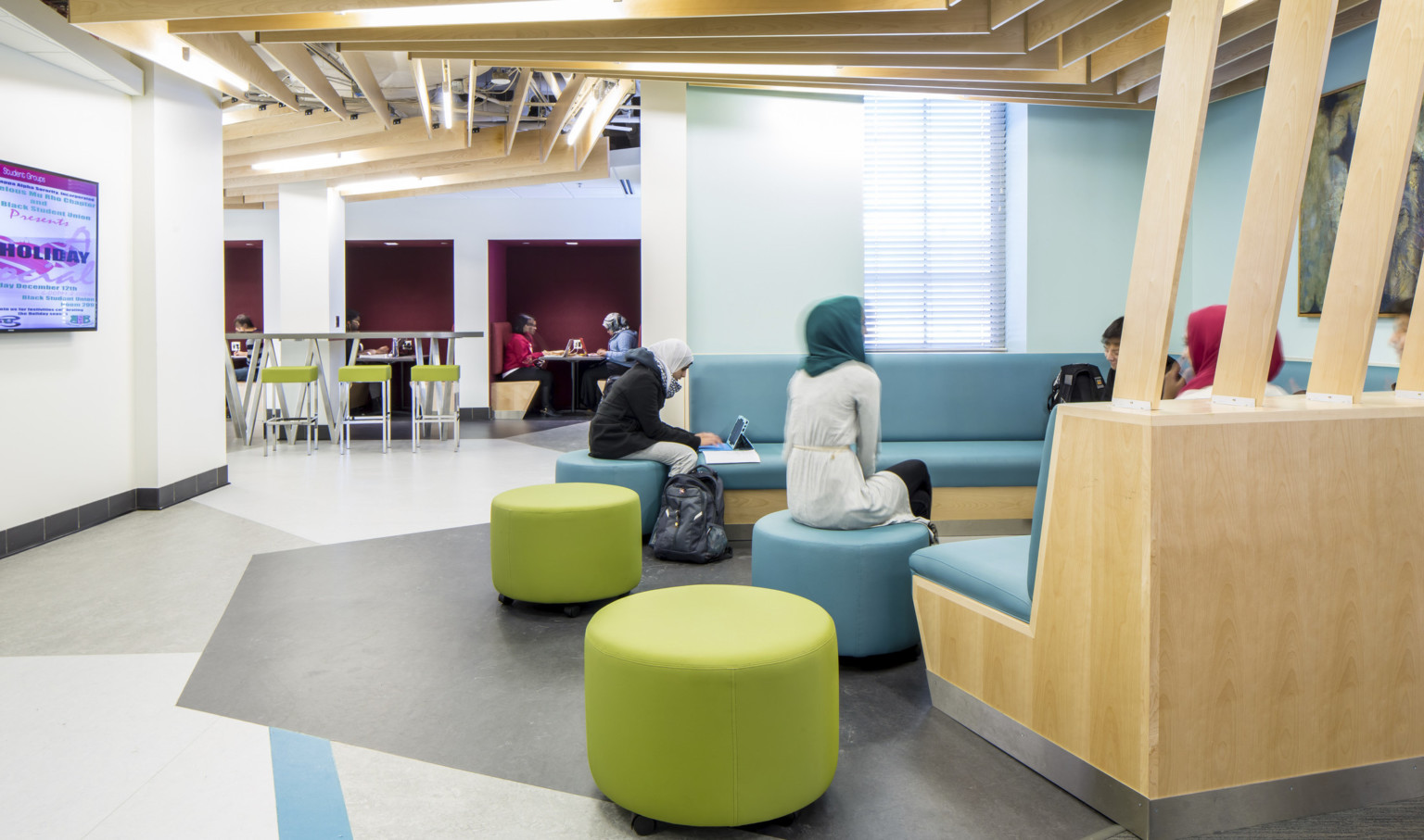 students working on blue banquette seating under a wood slat ceiling that wraps down to connect to back of booth in hallway