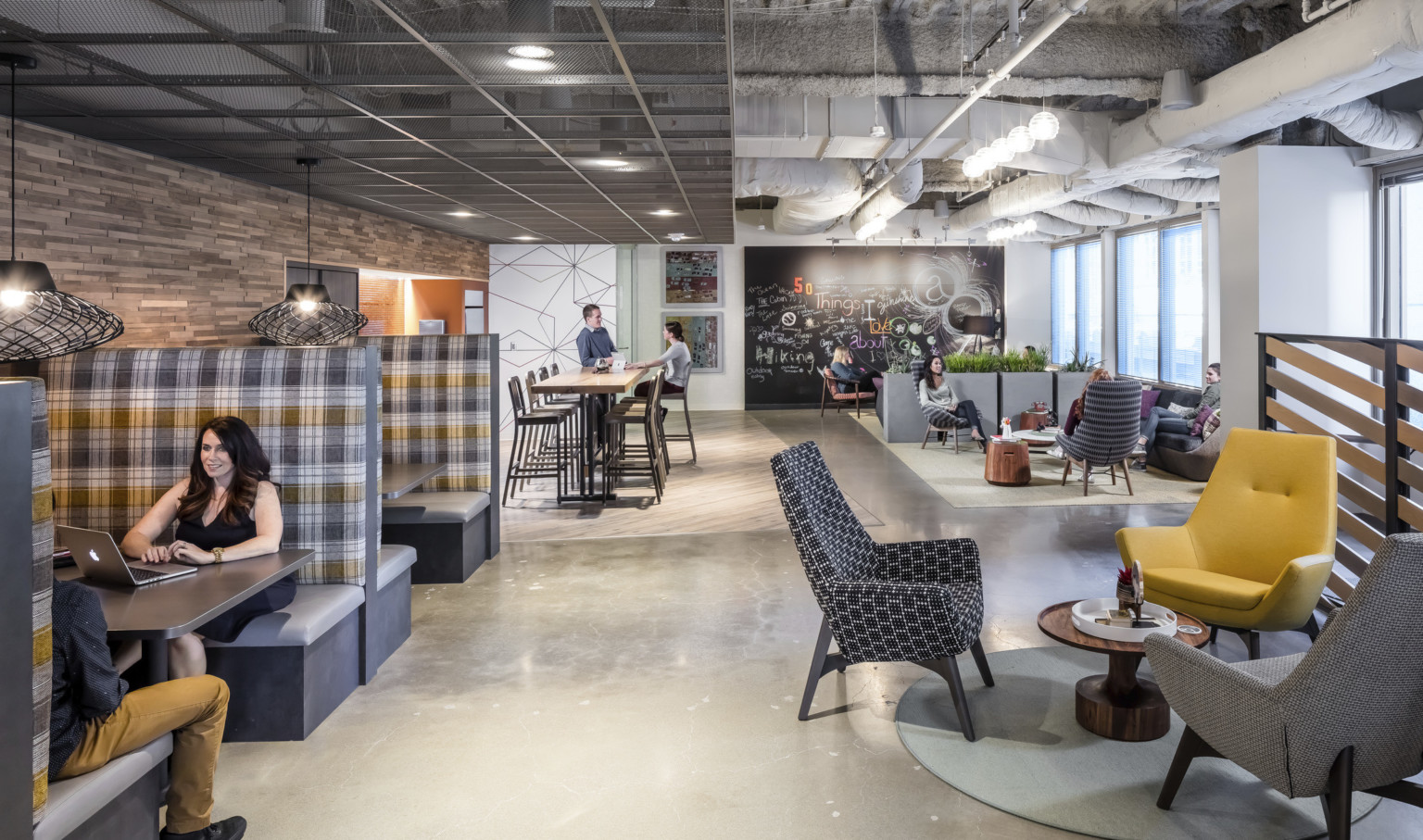 employee lounge and kitchen with plaid fabric booths and seating areas under exposed beams and ducts, metal grid left