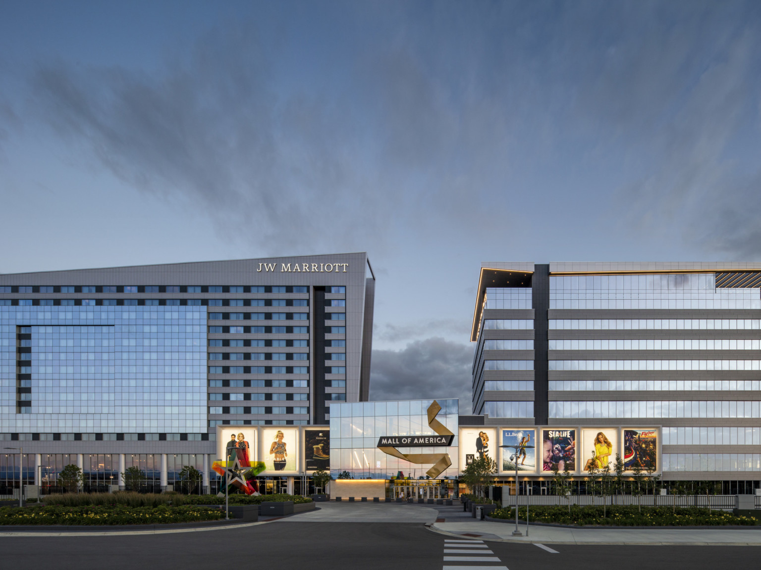 Mall of America entry with illuminated signage connects 2 grey angled buildings. Left building has JW Marriott written at top