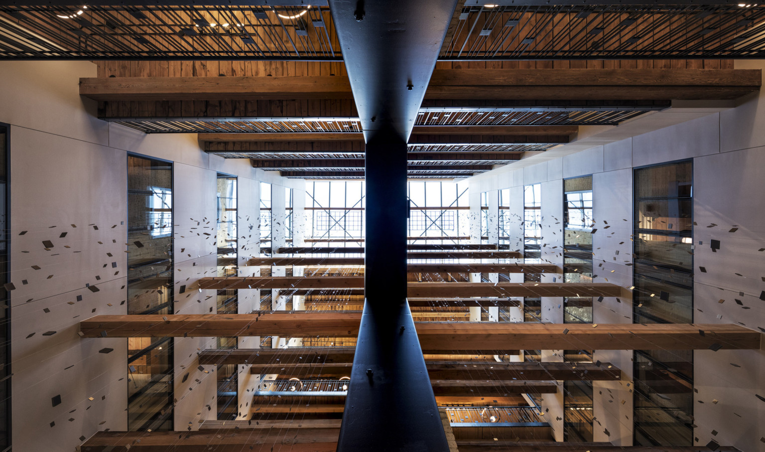 View of multistory atrium from above with walkways at each levels and wood beams between. Strung squares hang from grid above