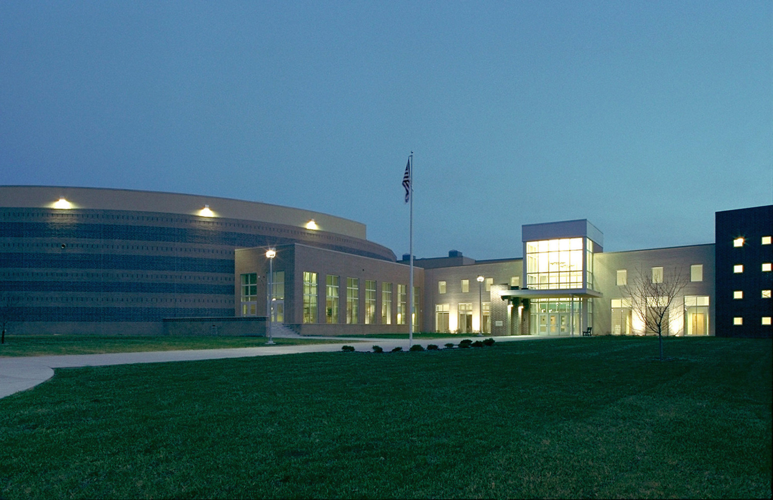 Exterior of Bemidji High School in Minnesota at night. Tall windows at entrance and along building are illuminated from interior