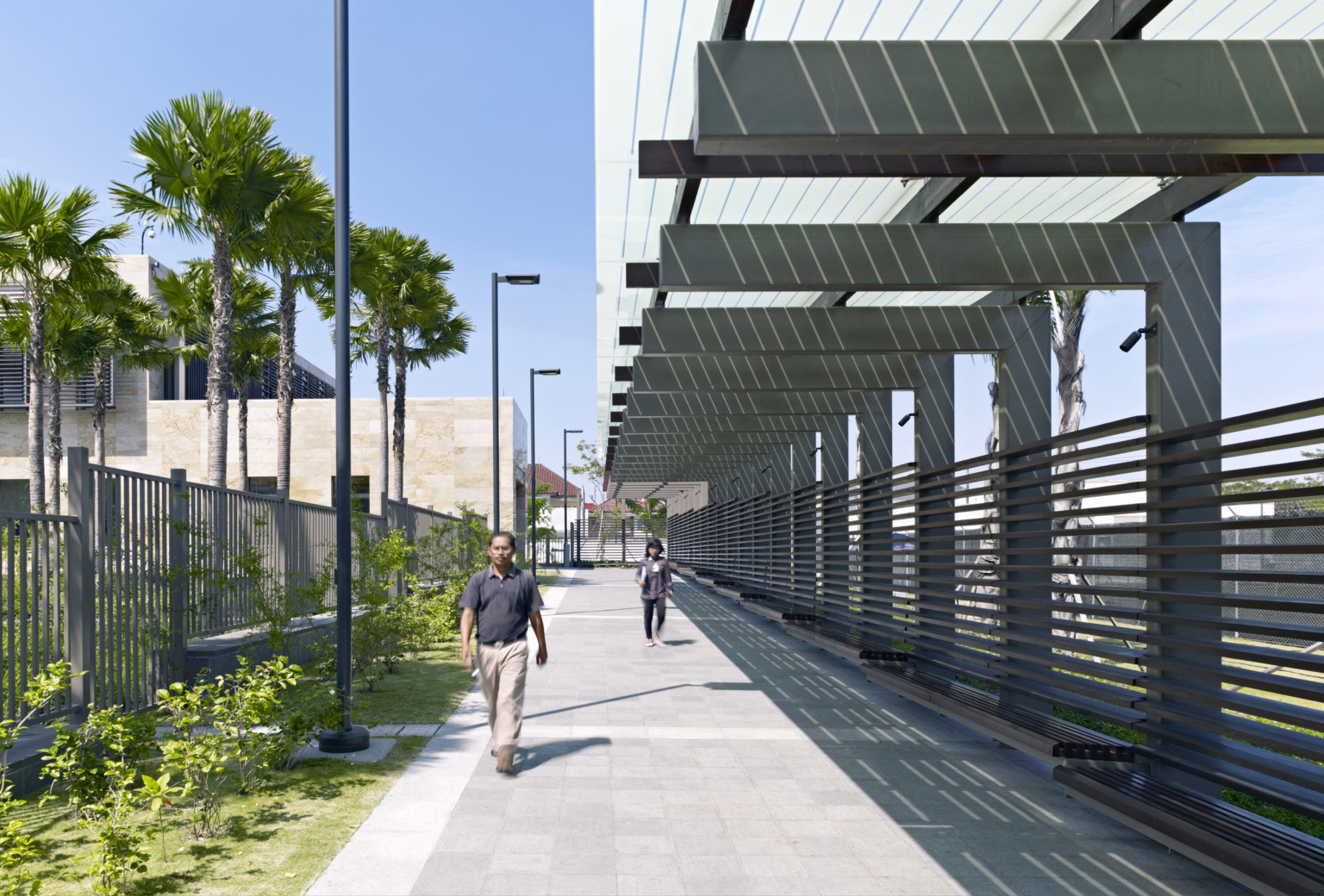 concrete brick path lined with vertical and horizontal fencing, perimeter has transparent canopy and slatted benches