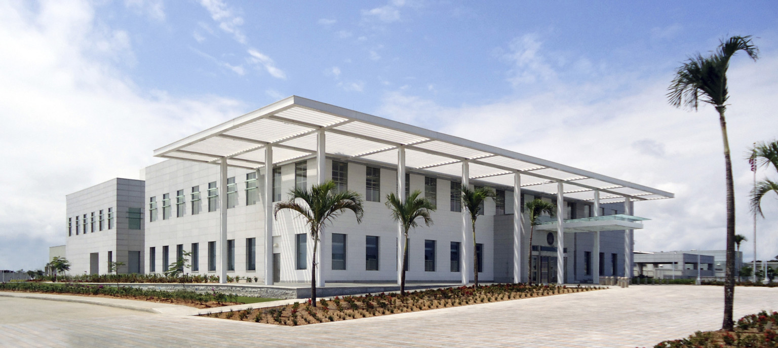 white symmetrically square two story building. a transparent shade over southern elevation and glass canopy over entrance.