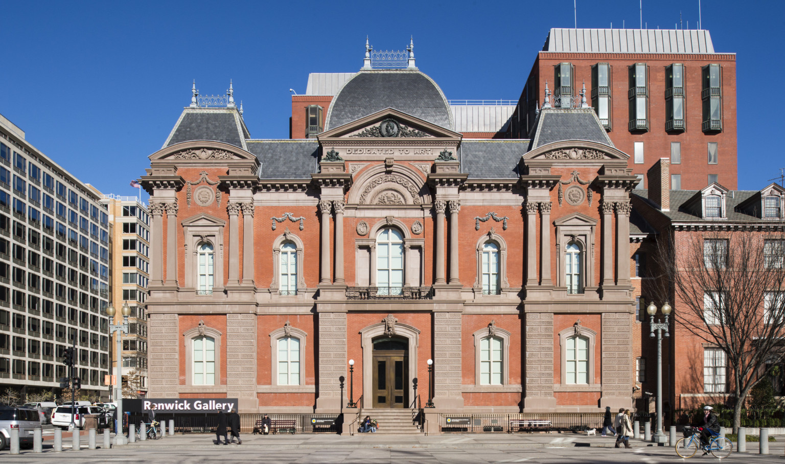 The front entrance to a two story red brick Second Empire style building with masonry and Dedicated to Art is carved at top