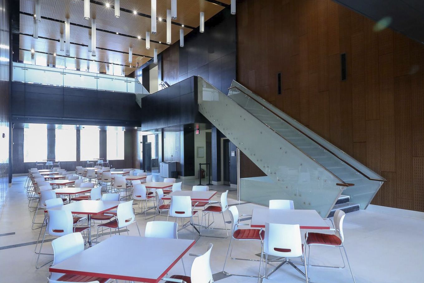 double height cafe with white floor and glass staircase. wood acoustic panel wall leads up to glass rail mezzanine level