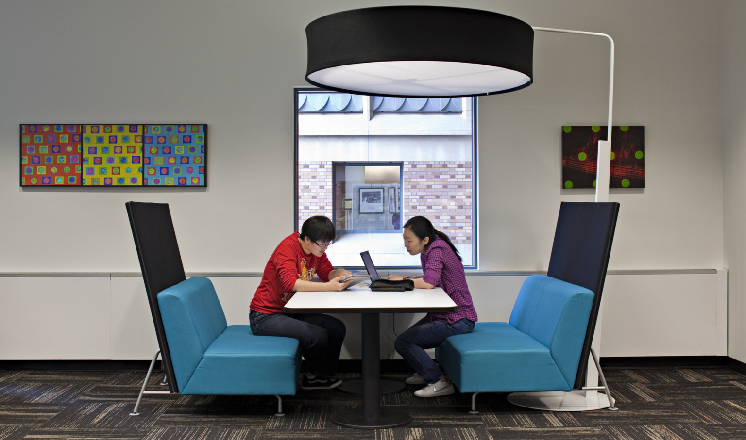 two students collaboration at a booth with blue chairs and large round floor lamp overhead at University of Washington