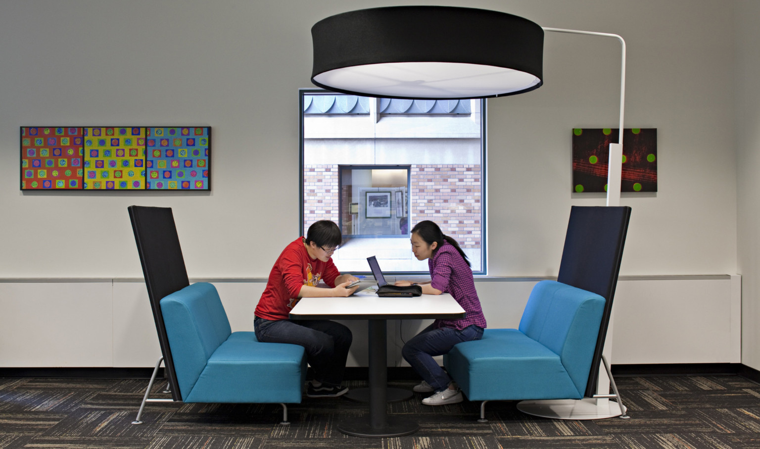 two students collaboration at a booth with blue chairs and large round floor lamp overhead at University of Washington two students collaboration at a booth with blue chairs and large round floor lamp overhead at University of Washington