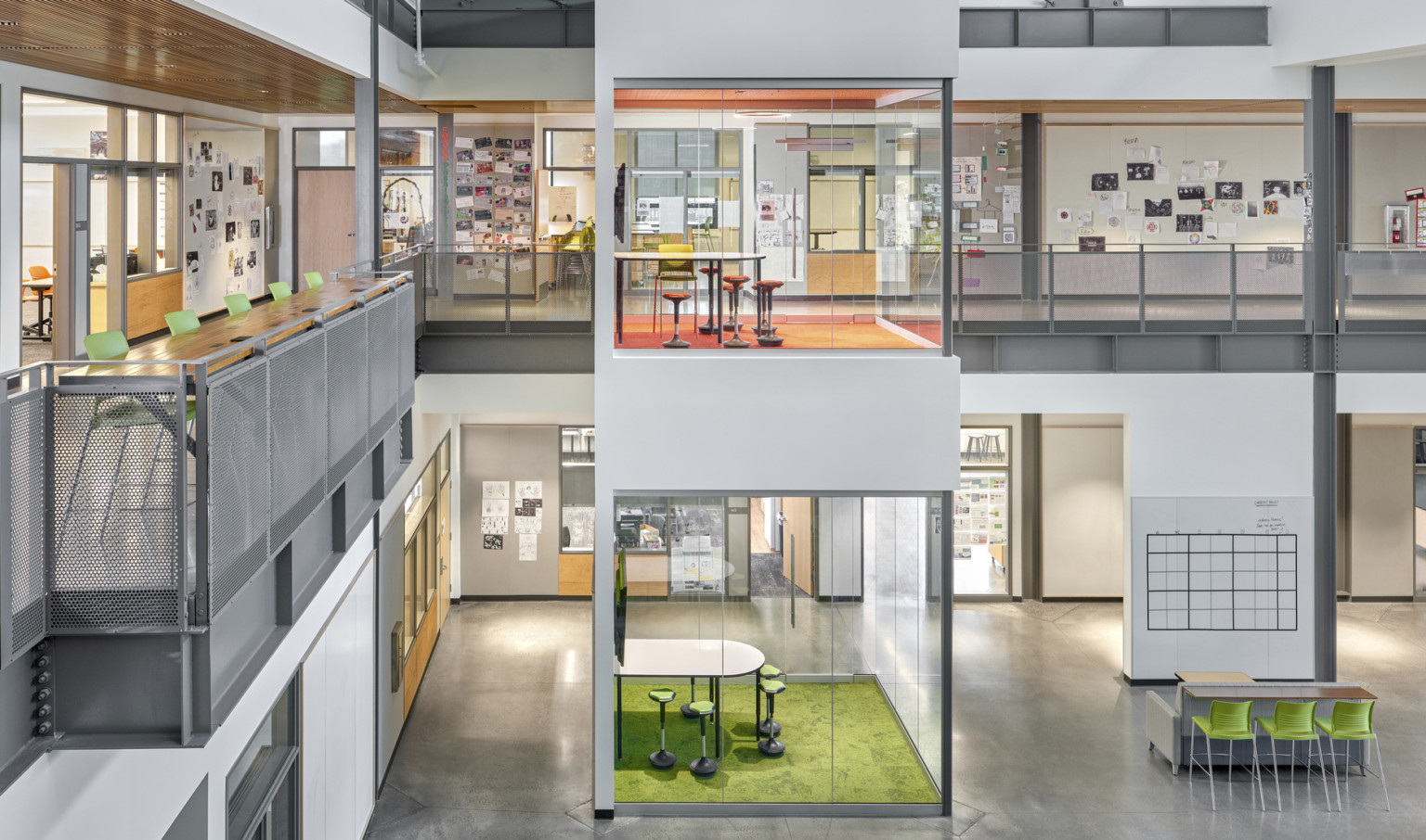 Viewed of atrium from the top of the stairs facing learning pods. 2nd floor hallway has wall collages and high top table