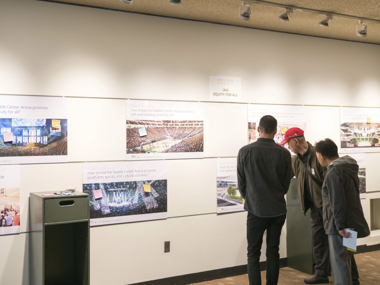 Three men pointing at a photo on white gallery wall in Seattle
