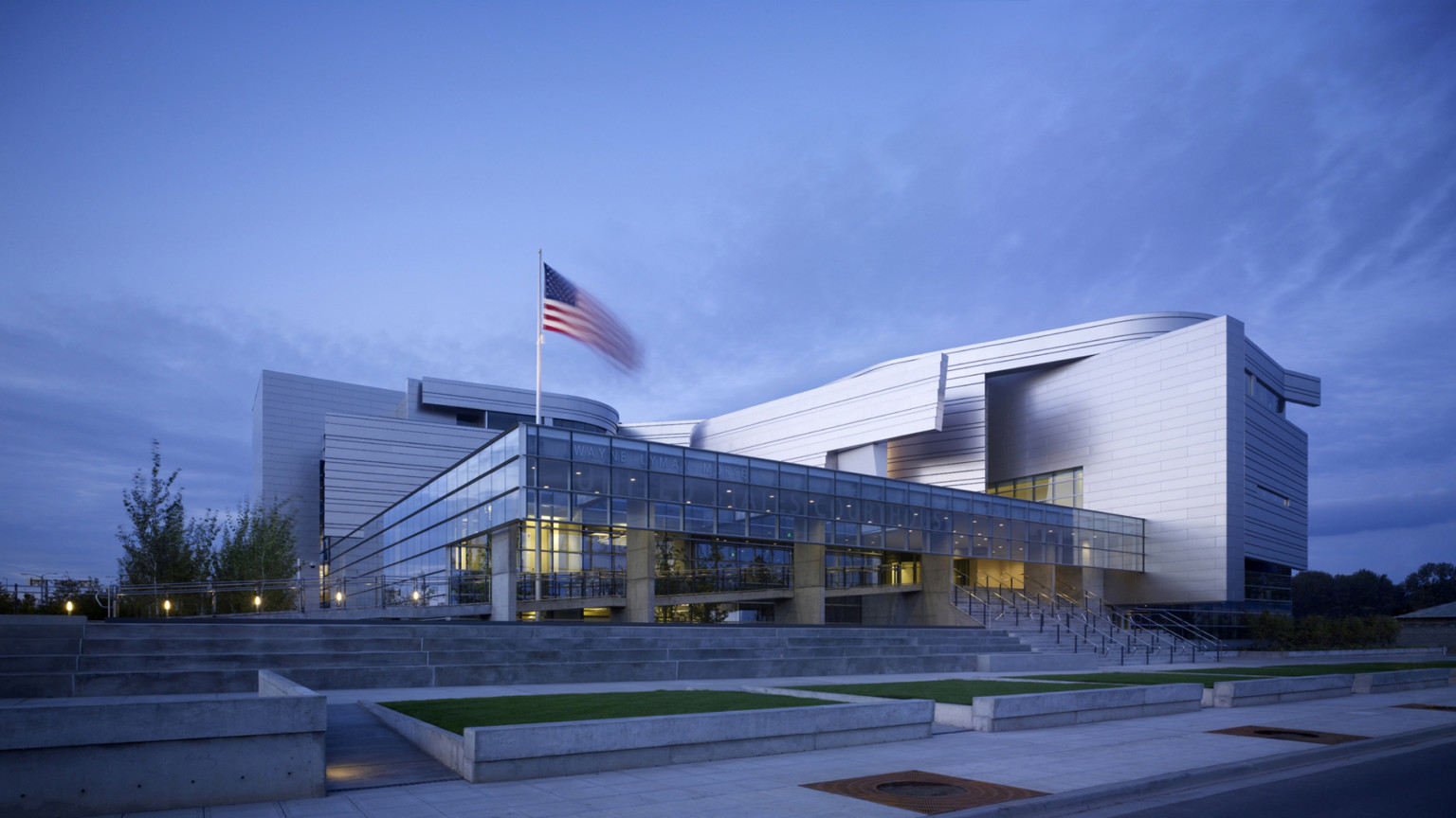 Night view of Wayne L Morse US Courthouse, a building with metallic curved facade and pillars supporting second-story overhang