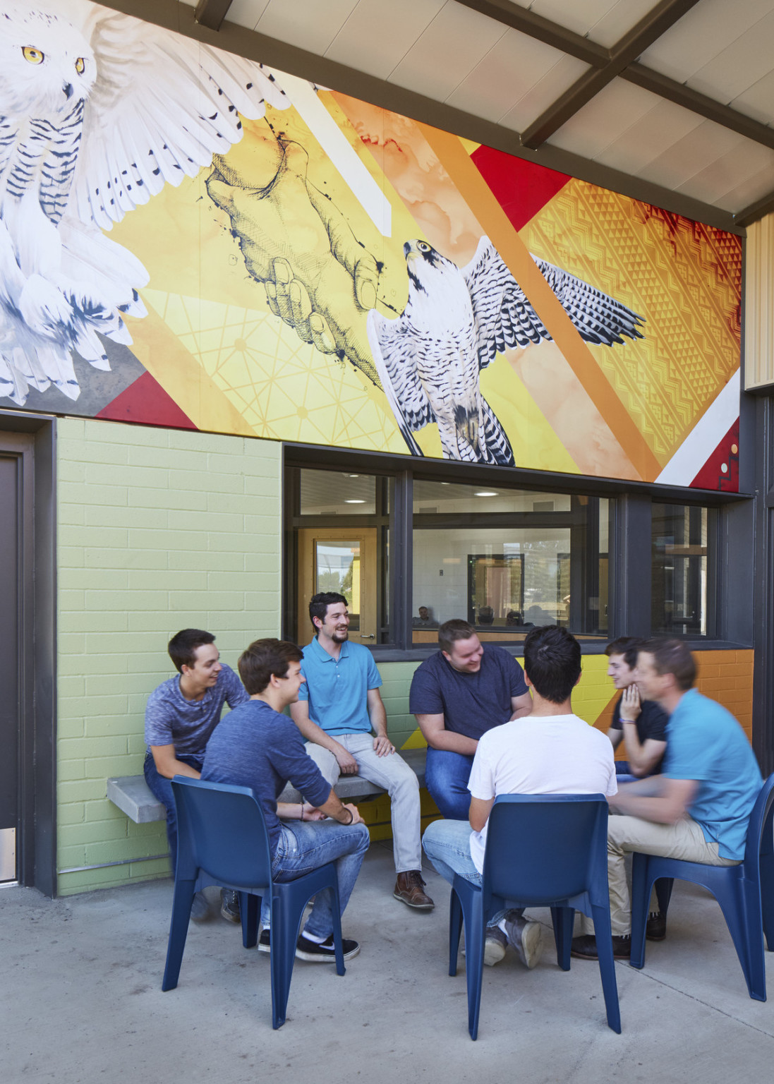 Seating against green, yellow, and orange colorblock wall with interior window. Above, a mural of owls, interlocking hands