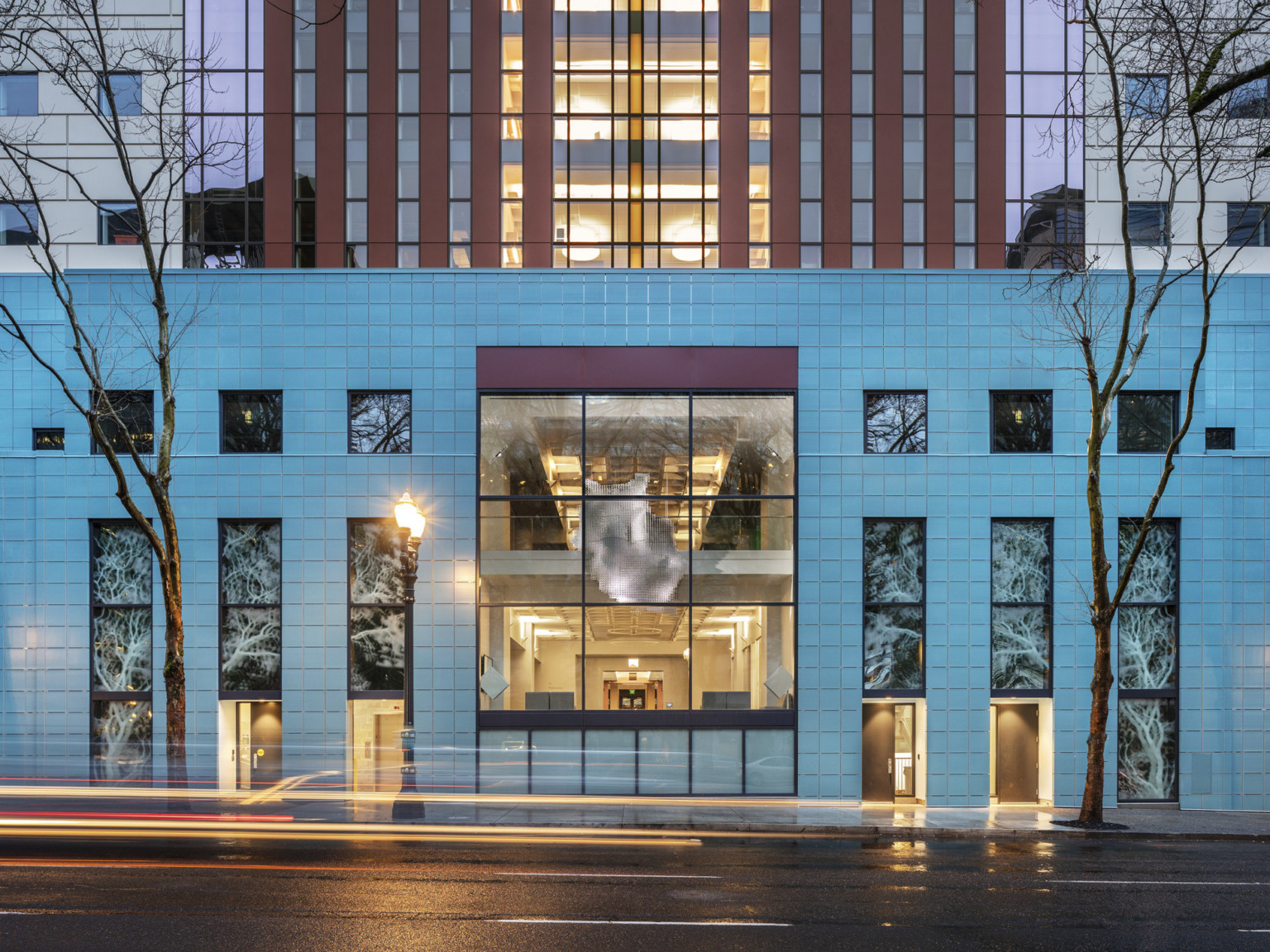 Exterior view at night of illuminated Portland Building with square window panels looking in to hung abstract art in atrium