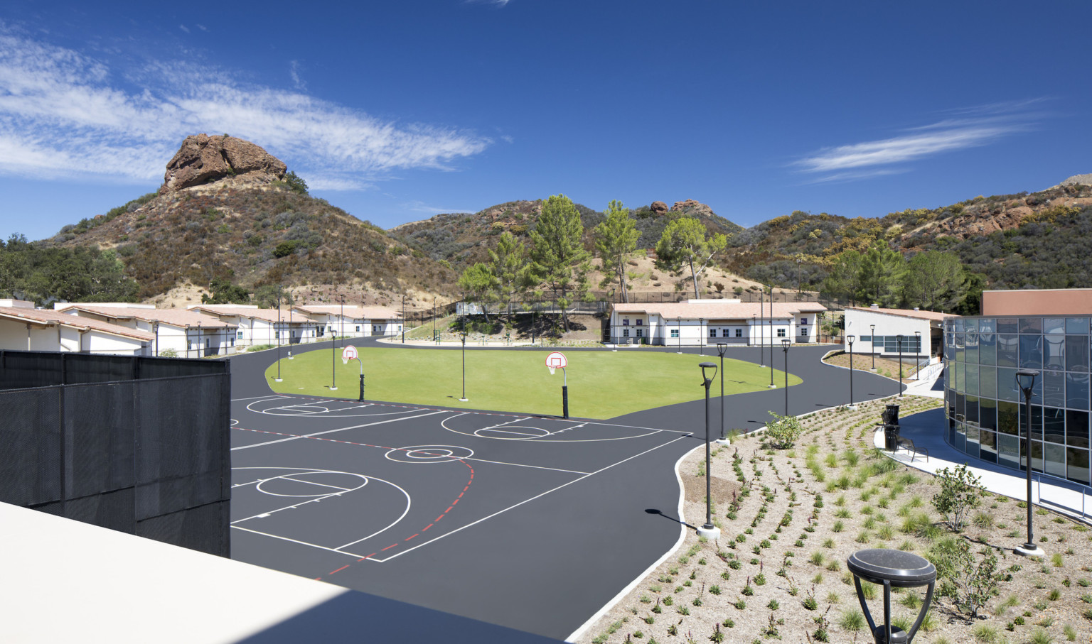 Rendering of a courtyard with basketball courts and a grassy area. Buildings along the back and right side. Hills beyond