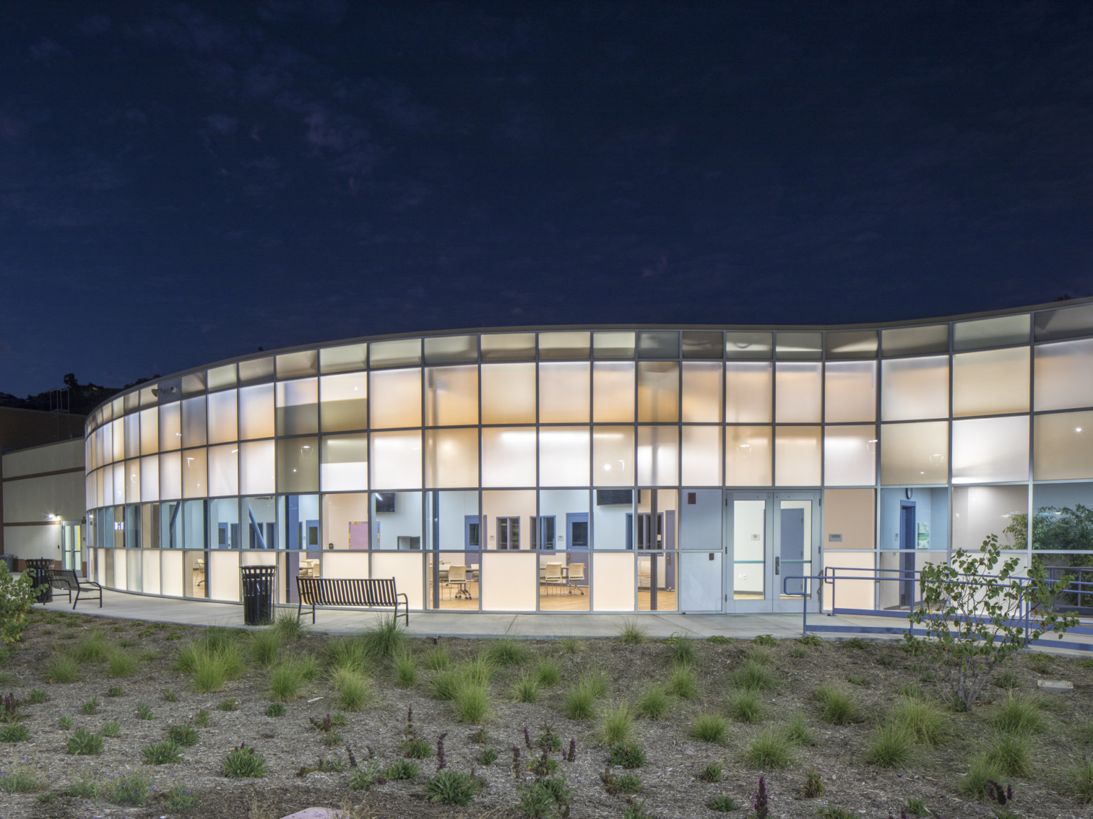 Campus Kilpatrick Youth Facility, an illuminated rounded double height paneled glass facade with blue translucent stripe