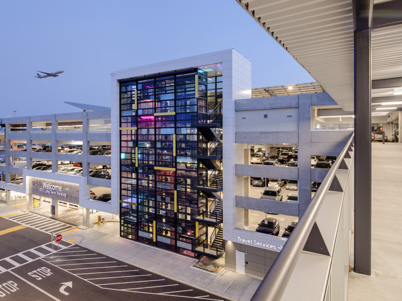 View from skywalk over road connecting to garage at 5th floor. Entrance to left, past glass tower. Plane flying above