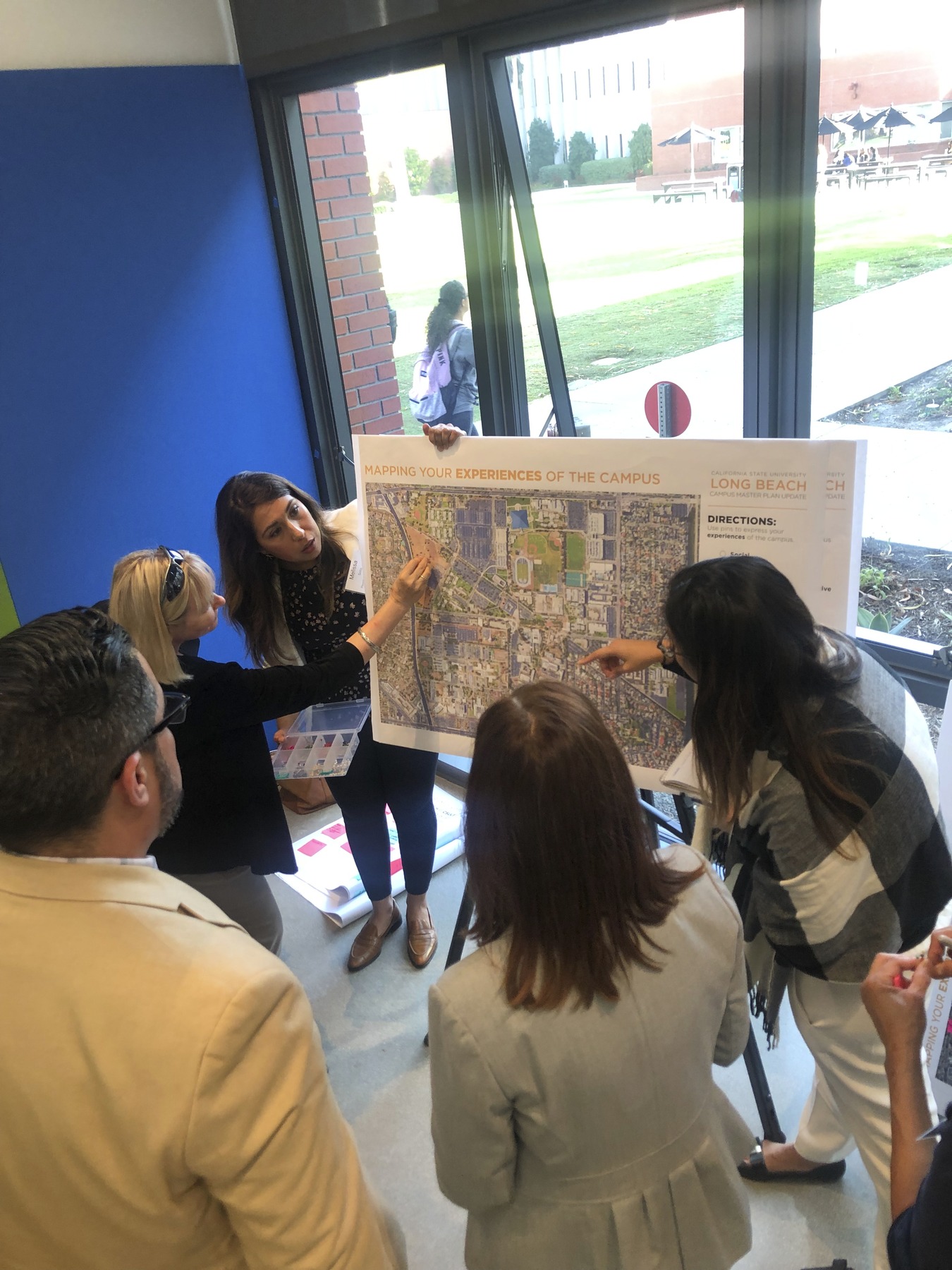 Engaged university stakeholders making notes on a campus map on a poster board and easel in front of floor to ceiling windows