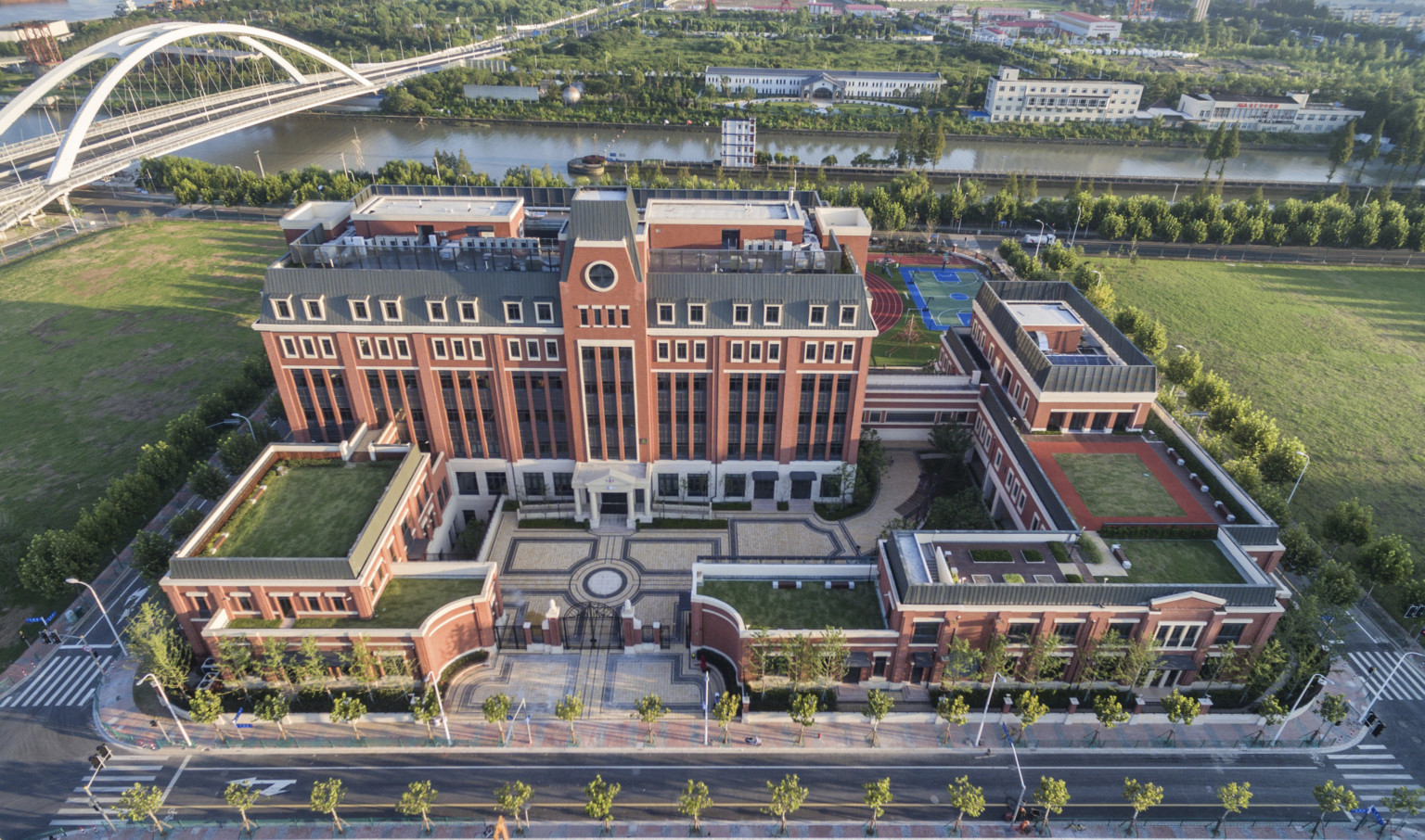 Aerial view of Huili campus from front. A gated stone courtyard is surrounded by brick buildings with living roof sections