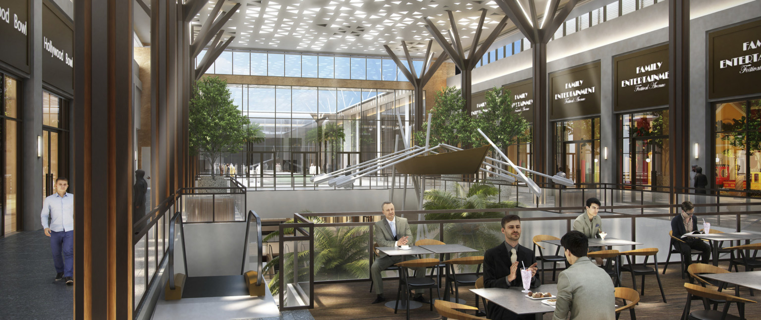 Seating area in atrium upper level. Shops along sides with double height glass wall, back. Panel with triangle cutouts above