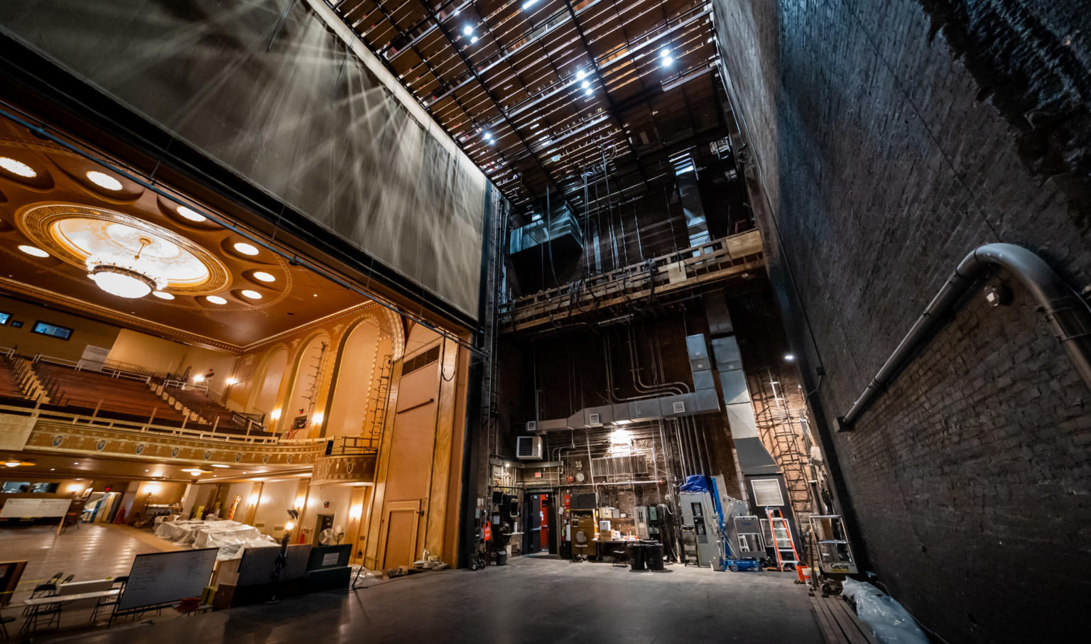 Backstage view of State Theater looking upwards to wood panel ceiling with light shining through. Bricks, right, seating left