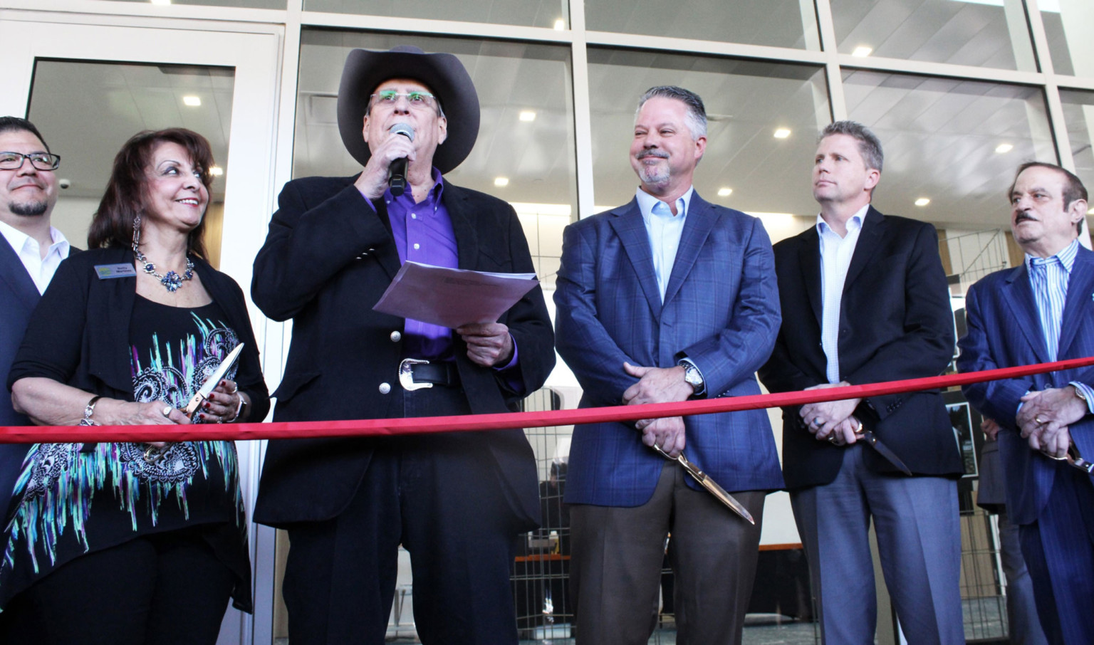 Pueblo Convention Center Expansion ribbon cutting with red ribbon in front of people talking and smiling