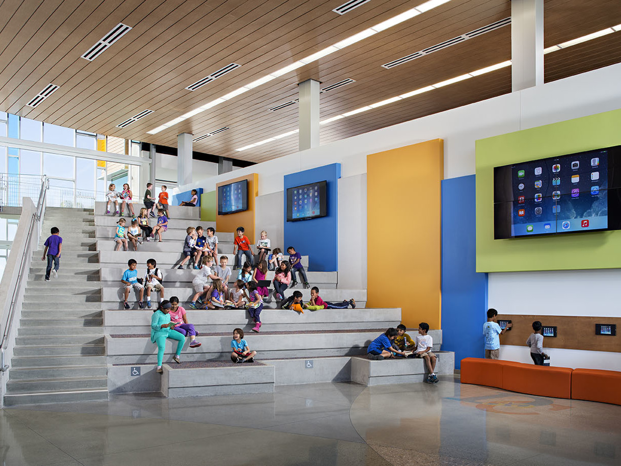 wood ceiling over concrete bleacher seating against a wall with blue orange and green panels and ipads and screens embedded