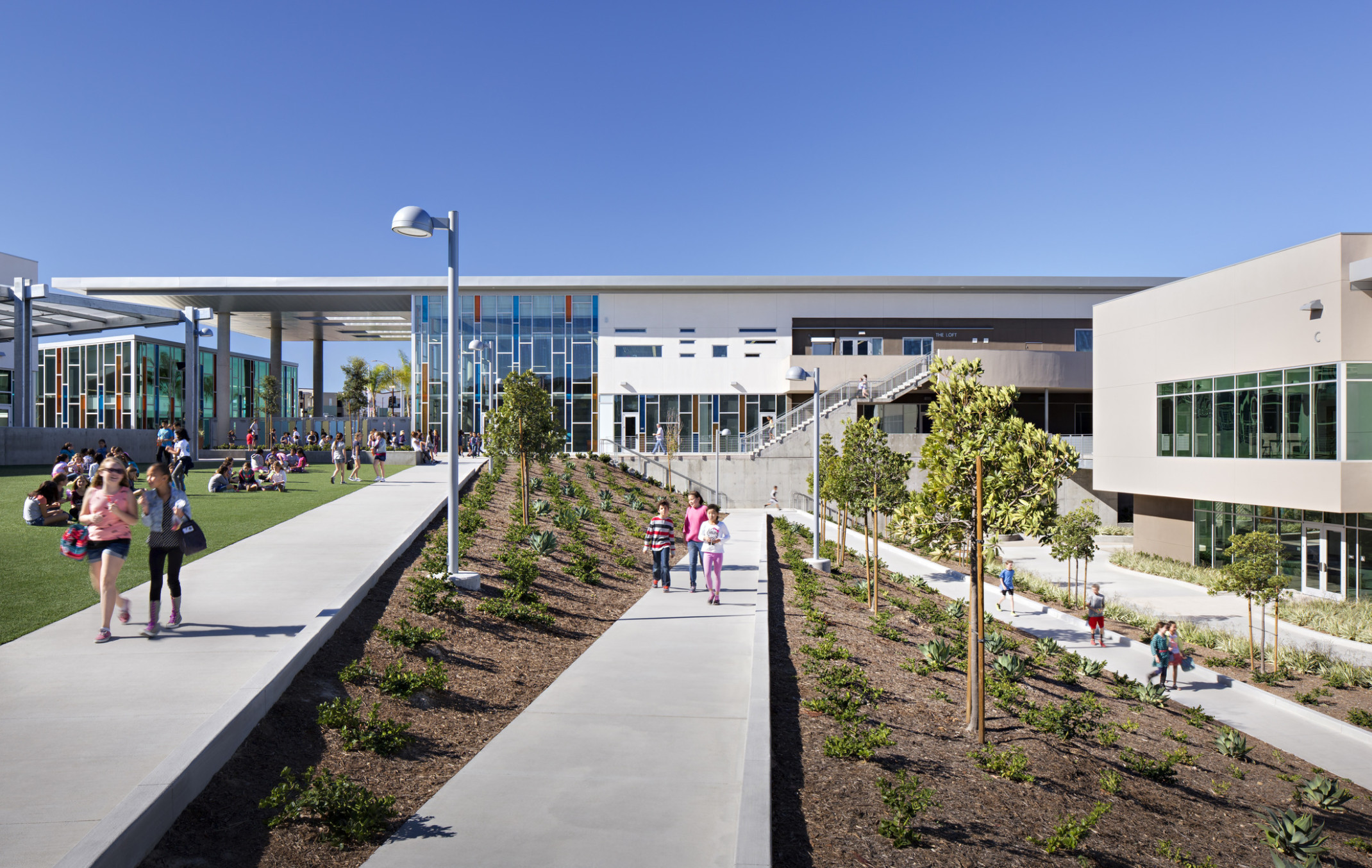 children walking on diagonal concrete paths between landscaping in front of Design 39, a multistory building with glass facade