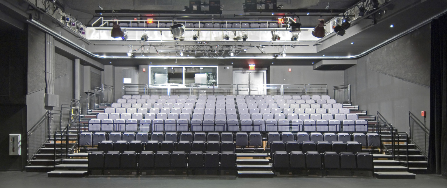 Two stories of stadium style grey seating in dark grey room with large light fixtures above