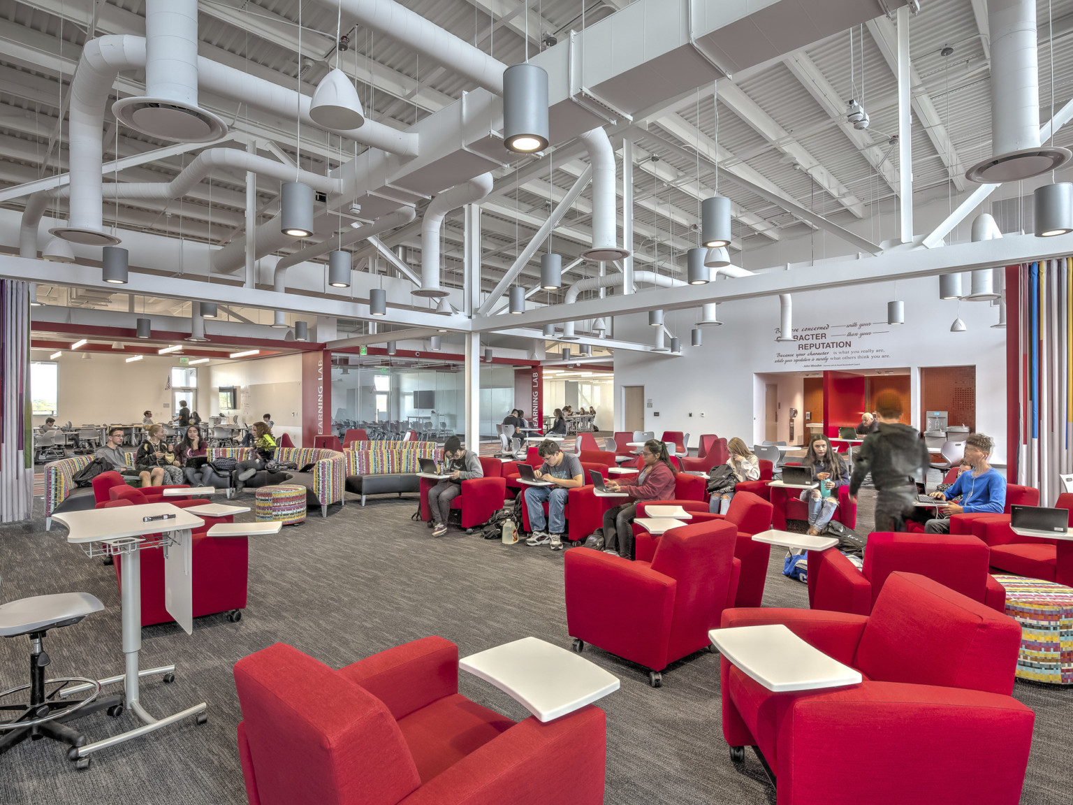 Large carpeted white room with red armchairs. Striped accent walls. Exposed ductwork and hanging pendant lights overhead