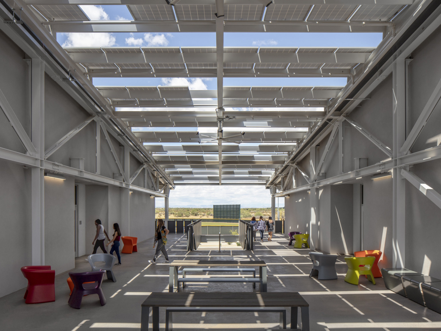 Solar panels stretch in rows between two white buildings, partially covering seating areas