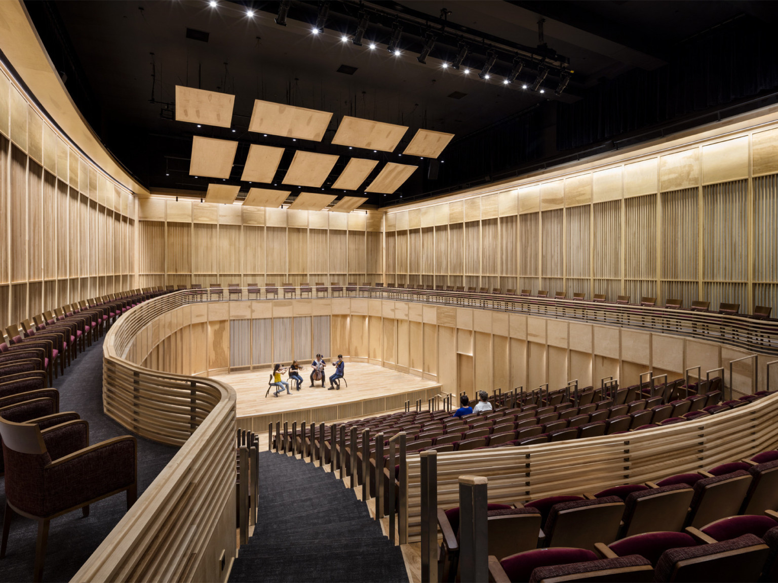 View from the back of wooden wall oval auditorium with 4 musicians on stage and 2 people seated in the audience