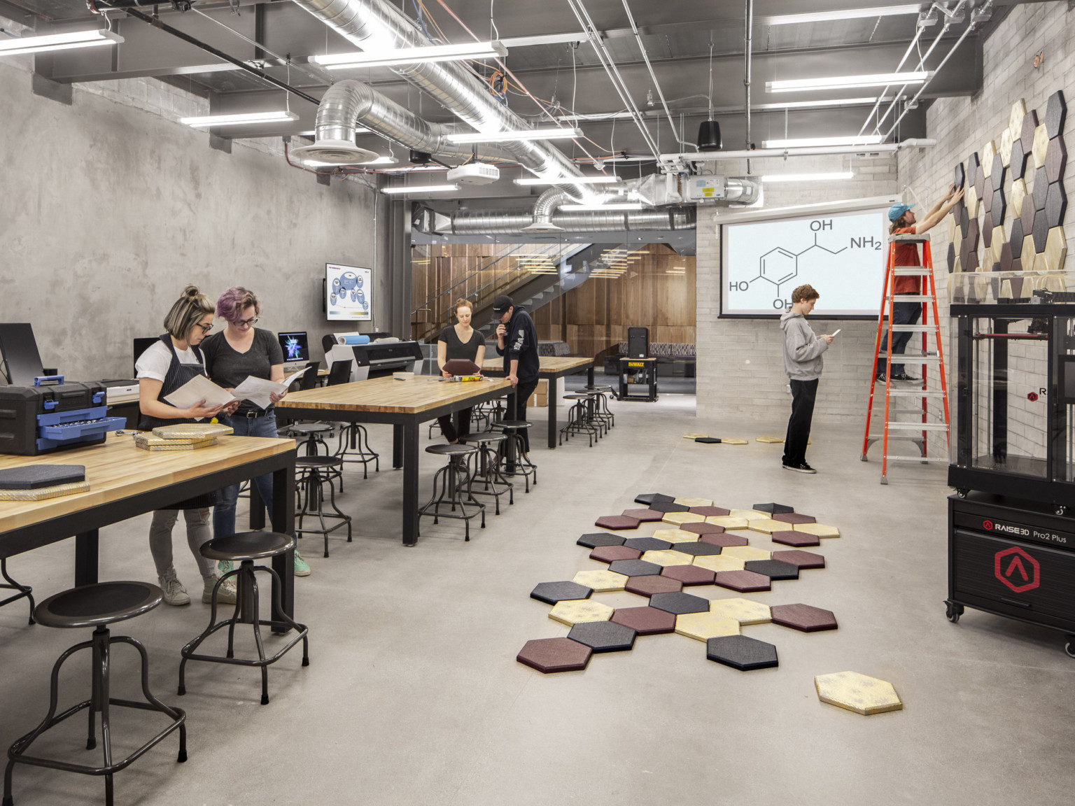 Students working with pentagon pieces in lab with long tables, computers, printers, and stools