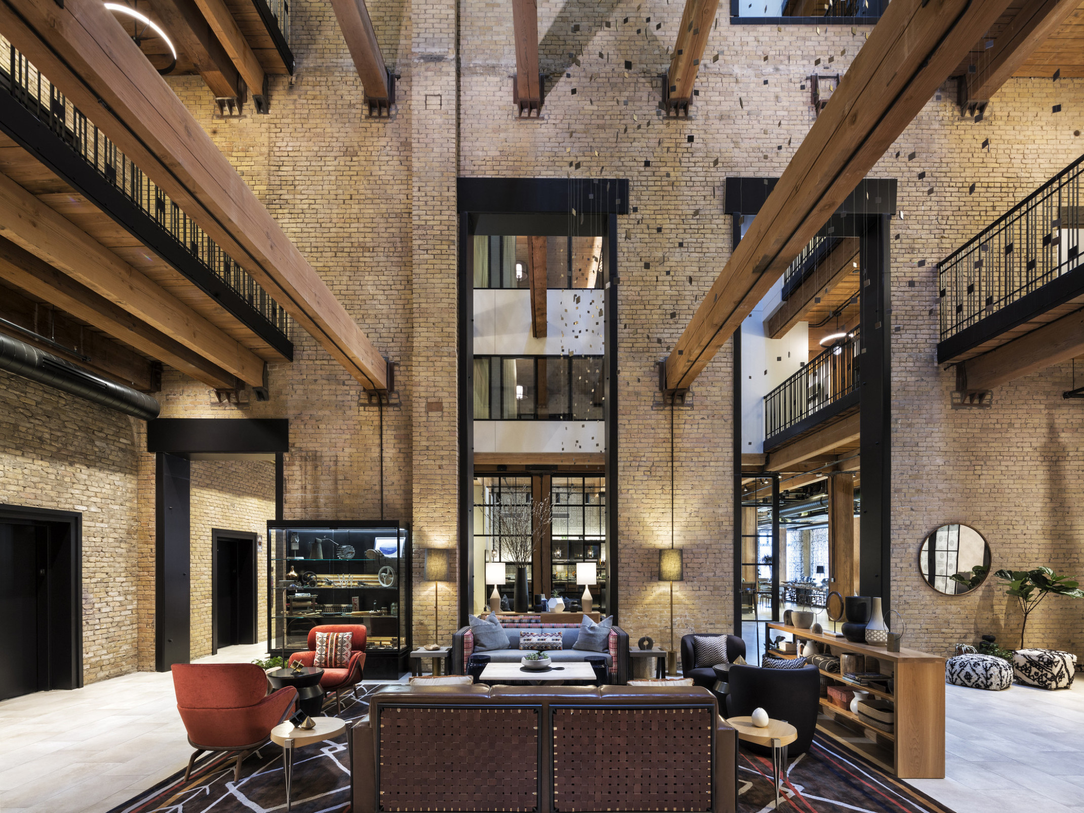 Interior atrium with exposed brick. Seating area at center and wood beams overhead. 2 walkways on sides above with metal rail, wood innovations grant, high performance design