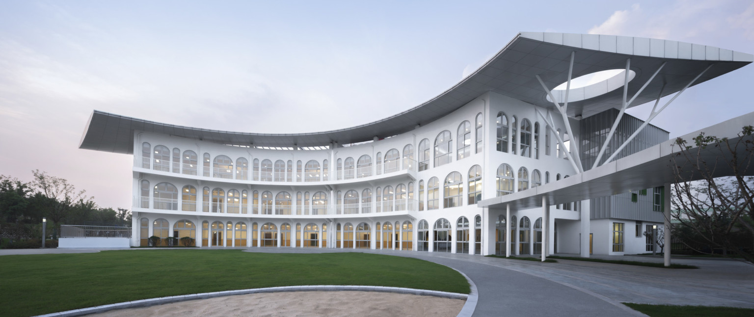 Side view of rounded front facade of white 3 story building with overhang, arched windows on each level, and balcony walkways