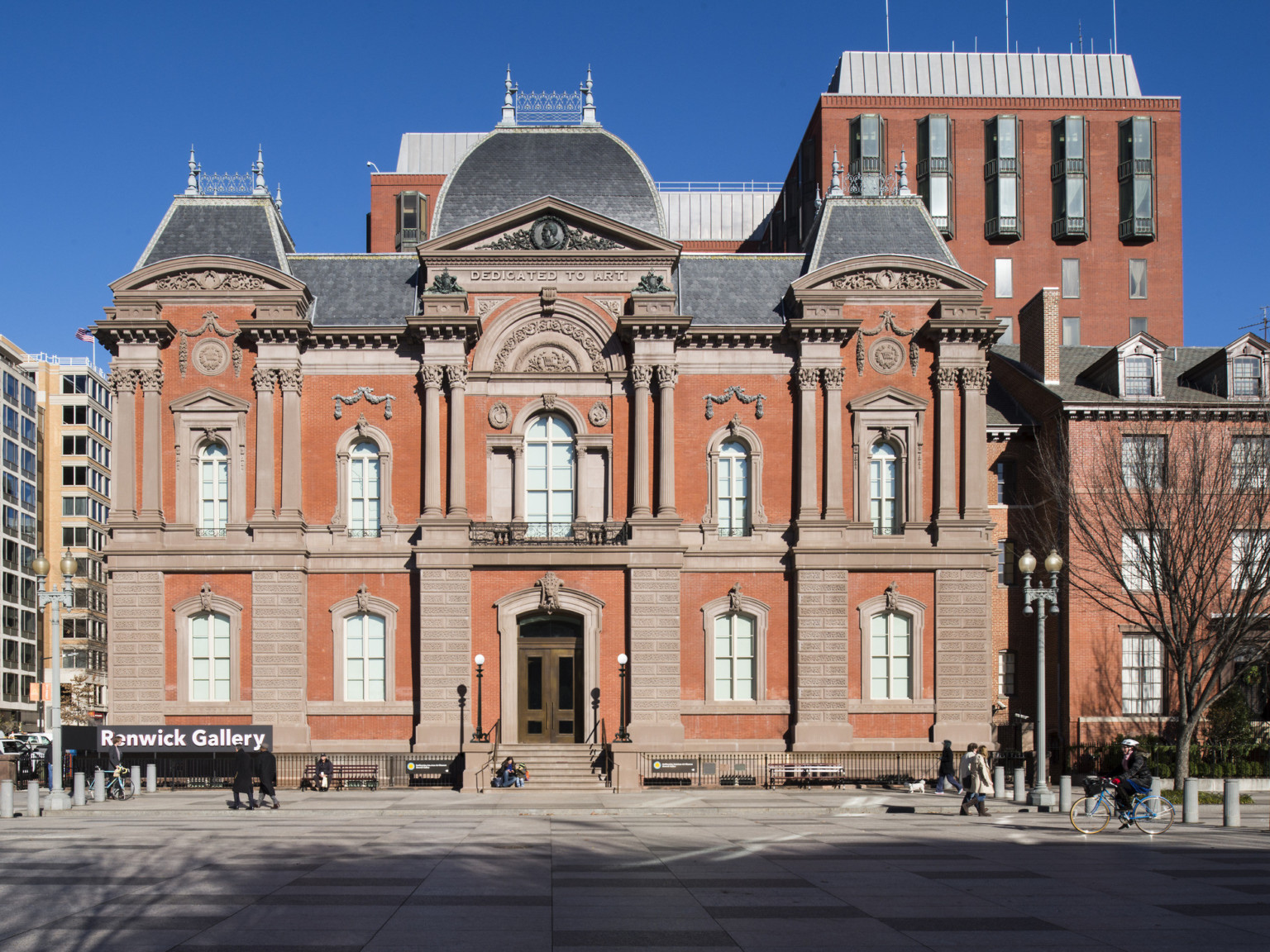 The front entrance to a two story red brick Second Empire style building with masonry and Dedicated to Art is carved at top