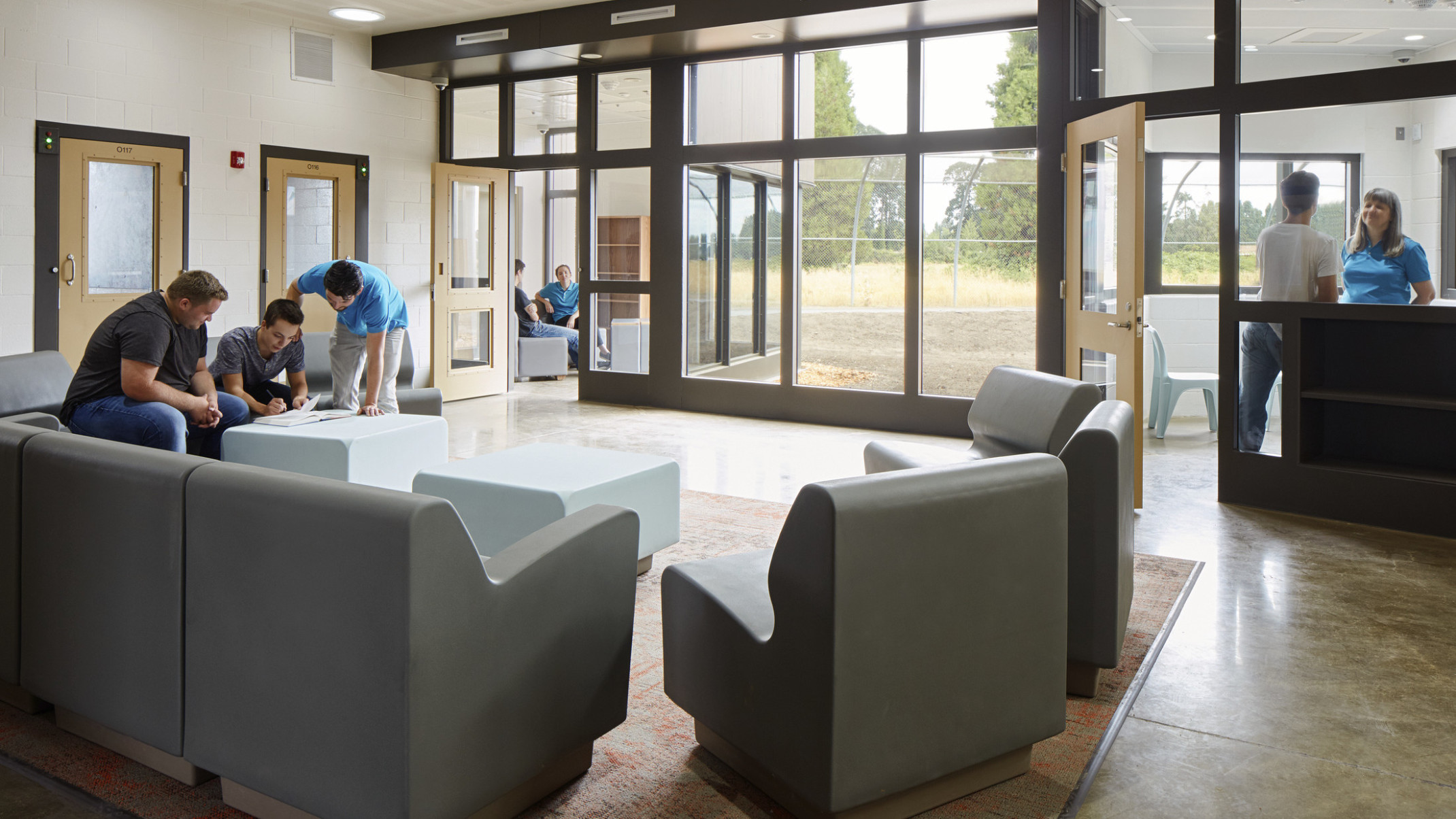 seating area inside Oregon Youth Authority MacLaren Campus with people gathered around grey lounge chairs