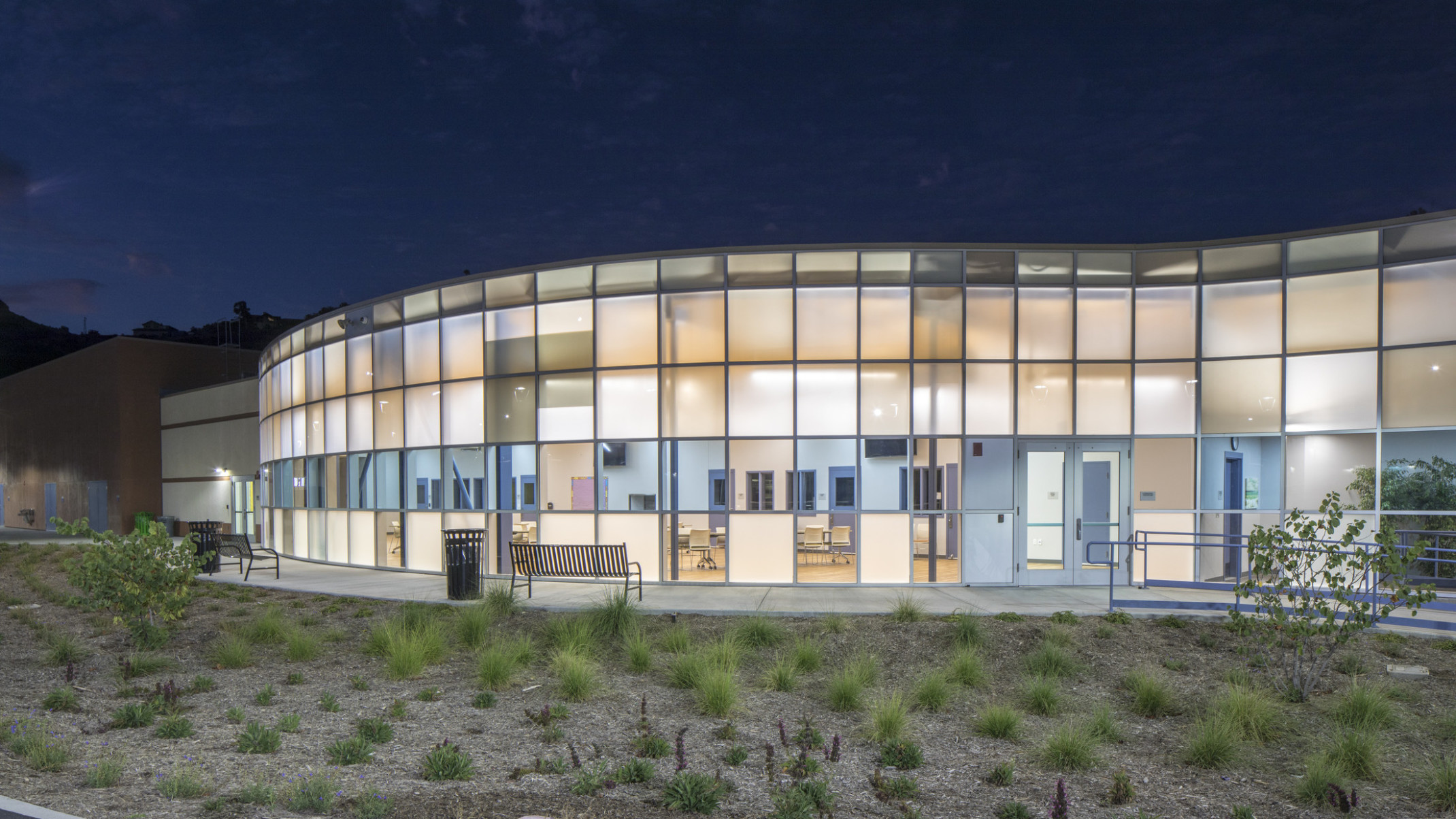 Campus Kilpatrick Youth Facility, an illuminated rounded double height paneled glass facade with blue translucent stripe