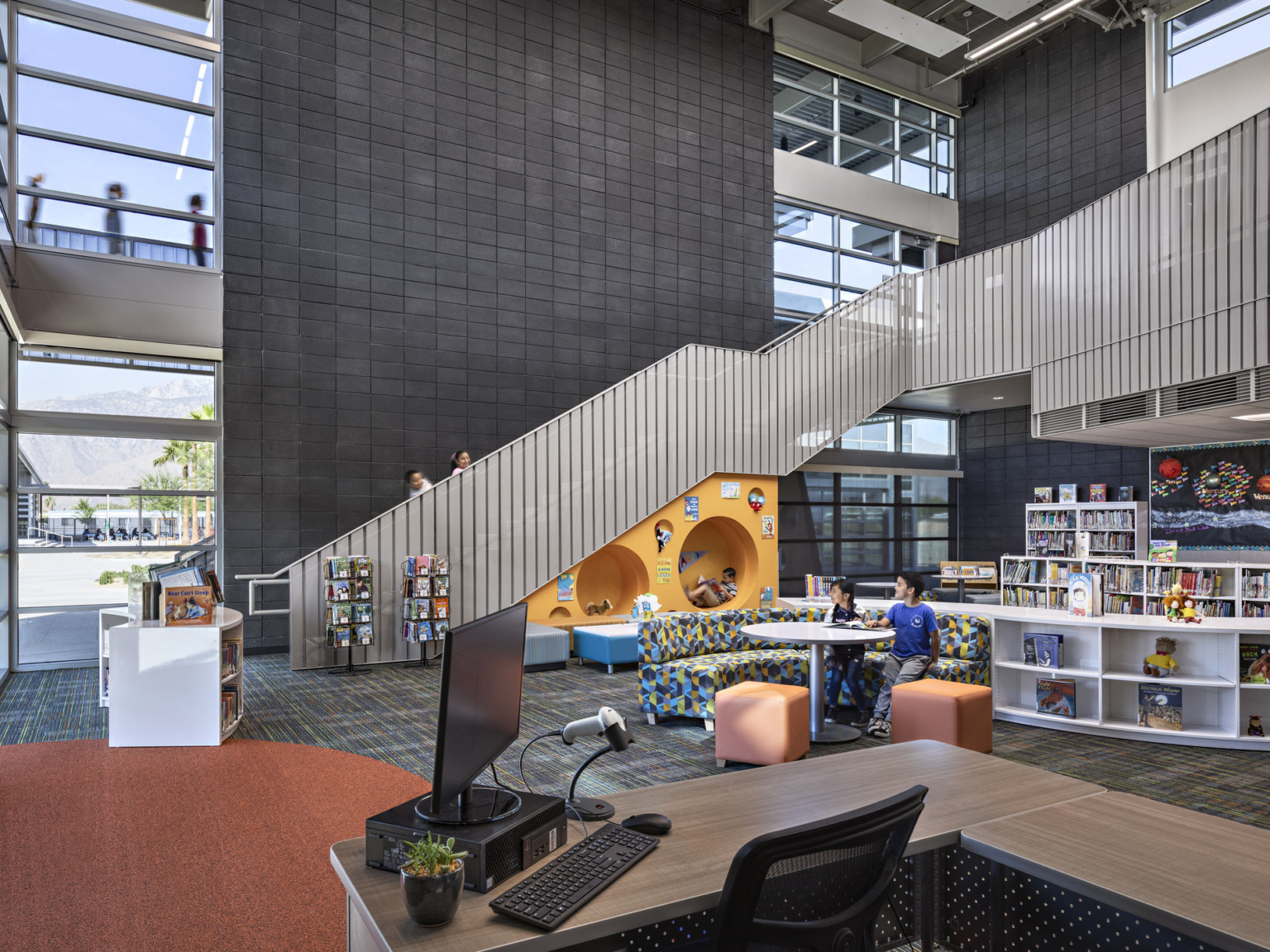 Triple height library with rounded white half height bookshelves and patterned couch. Orange accent wall with round cutouts