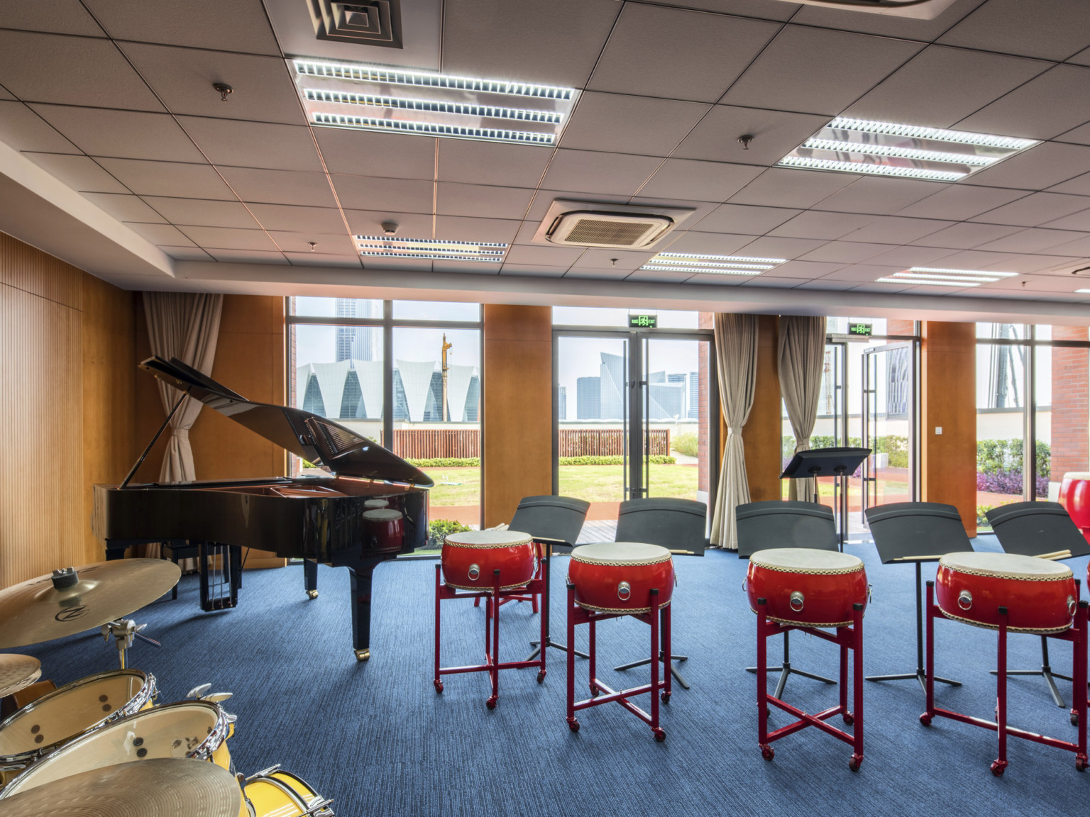 A music room with wood walls, floor to ceiling window panels, and glass double doors opening out to the lawn with a city view