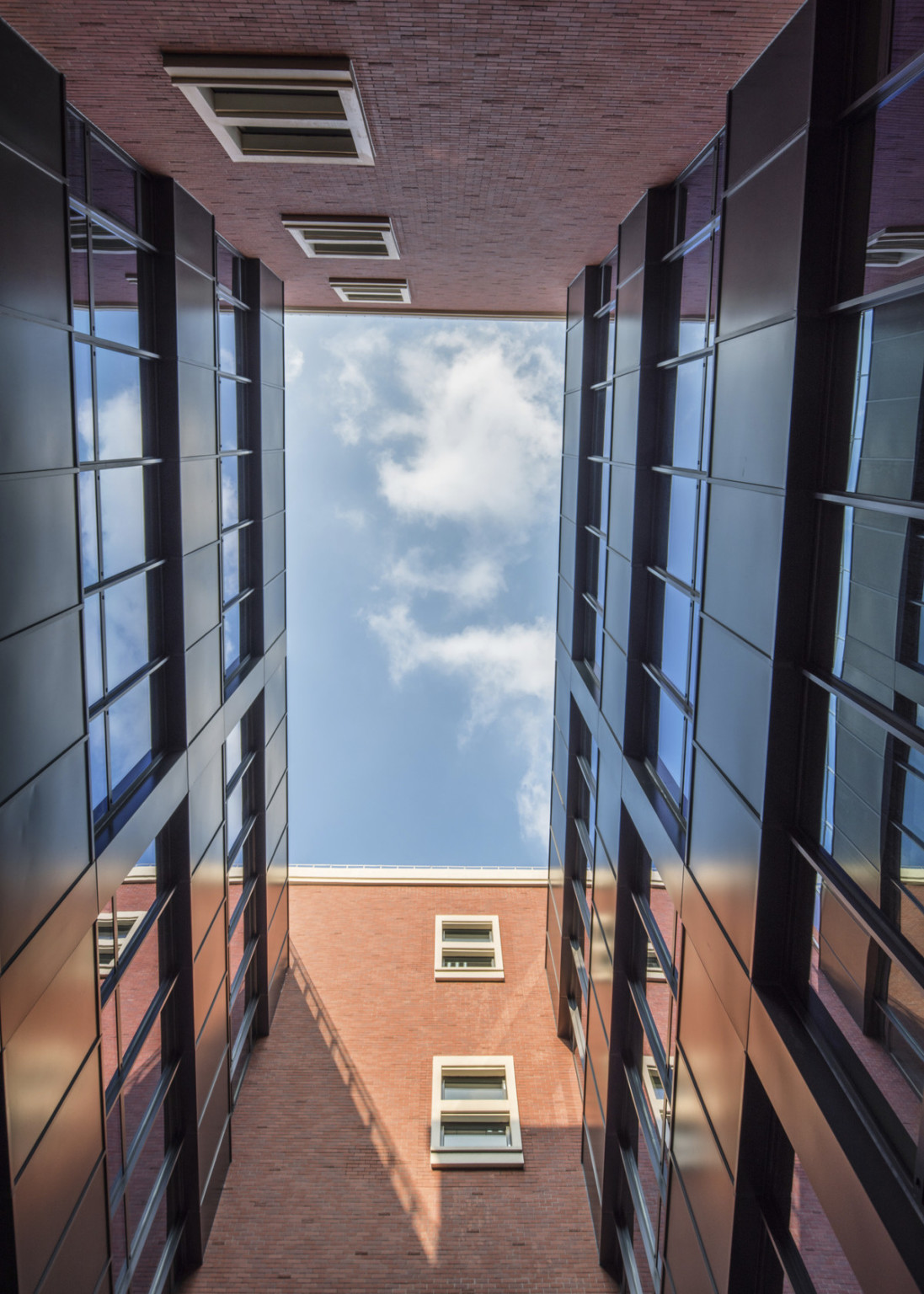 View between buildings looking upward. Brick walls with white windows, front and back. Black walls with windows, either side