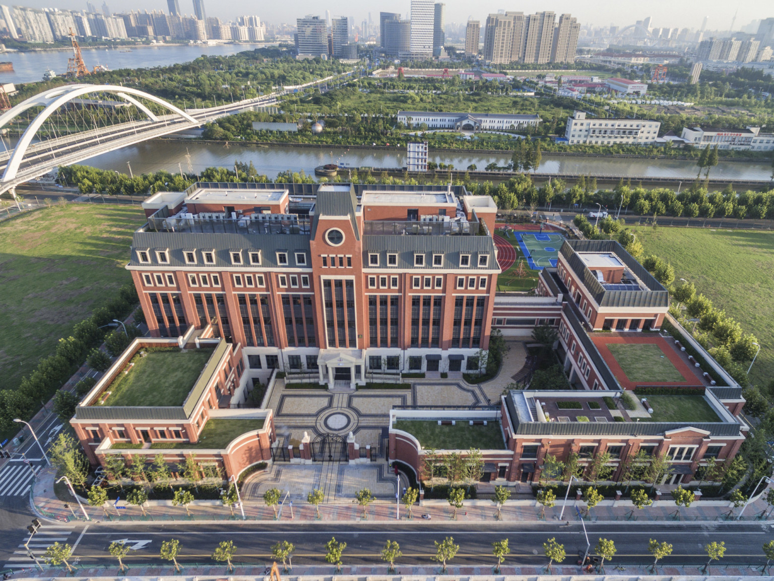 Aerial view of Huili campus from front. A gated stone courtyard is surrounded by brick buildings with living roof sections