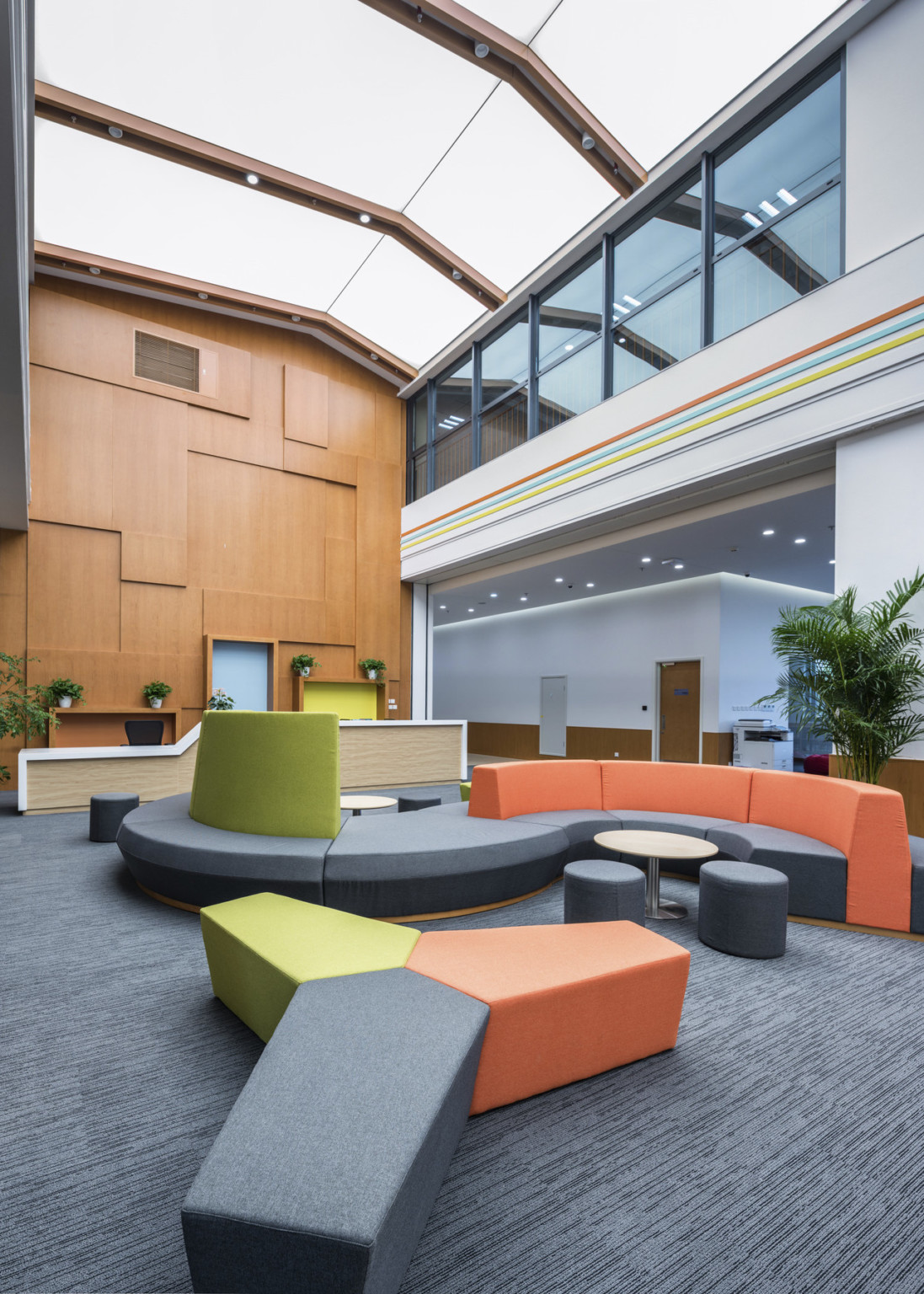 Double height atrium with ergonomic seating area. A multicolor curved couch with matching benches. Right, a 2nd floor walkway