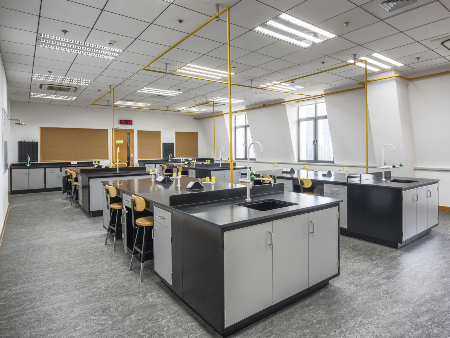 Science lab with partitioned sinks at ends of lab tables. Tables have black counters and grey drawers divided by yellow chair